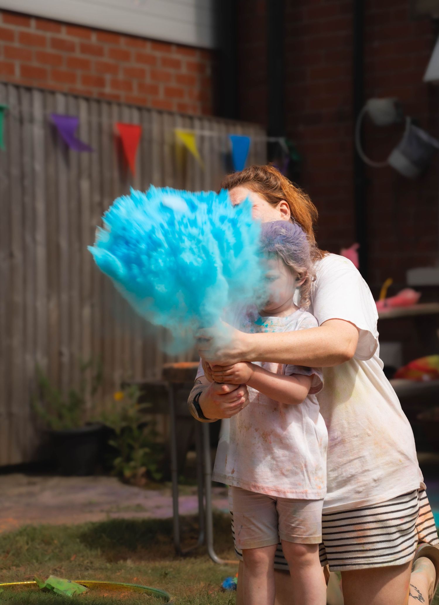 Woman and child playing with blue powder paint explosion in a sunny backyard during a party.