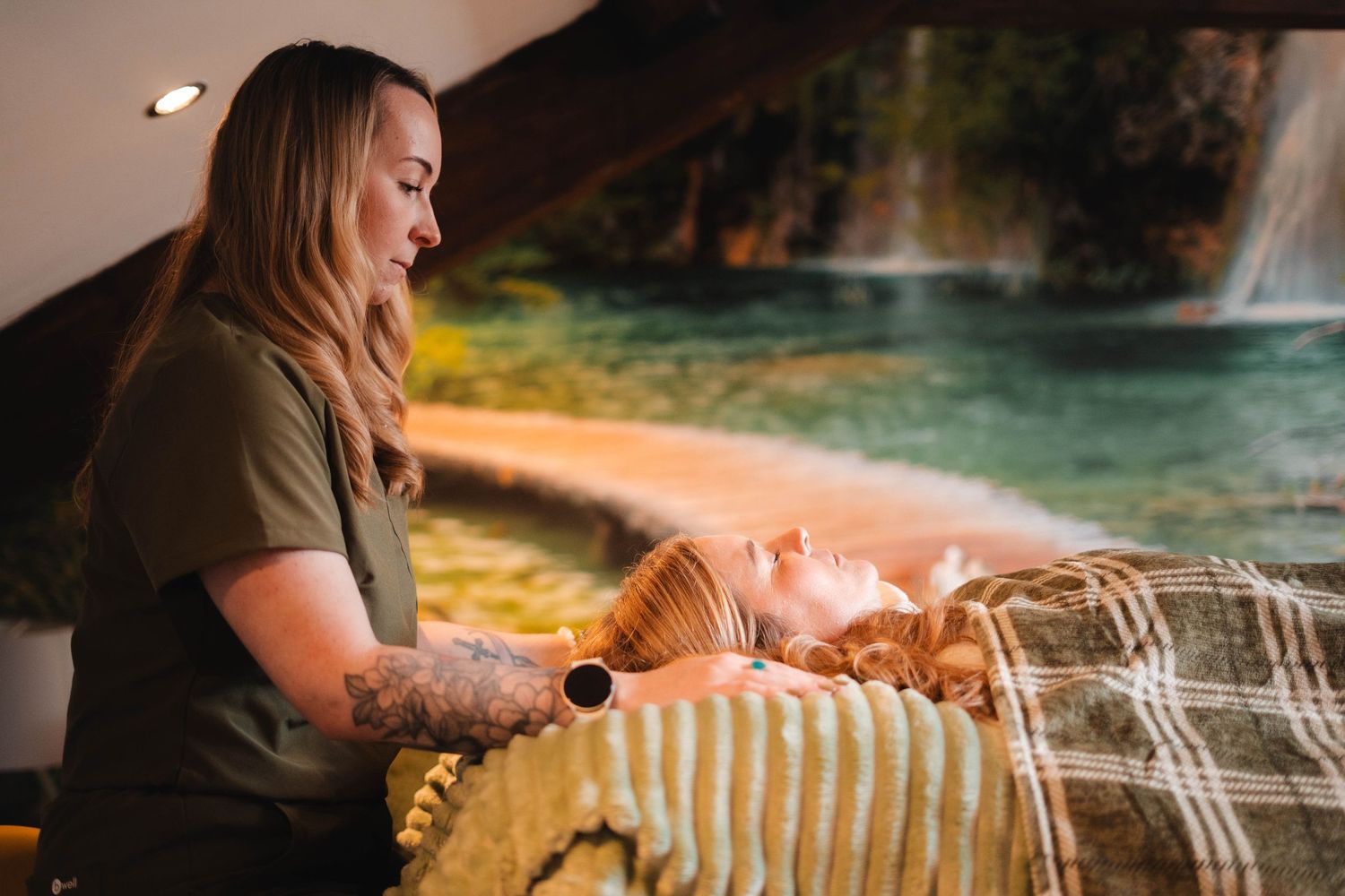 Female therapist in olive scrubs performing Reiki energy healing on a client in a spa room.