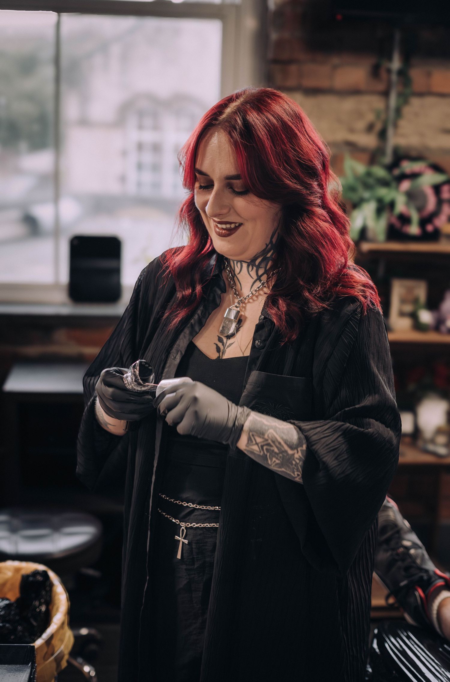 Red-haired female tattoo artist wearing black gloves prepares equipment in a tattoo studio.