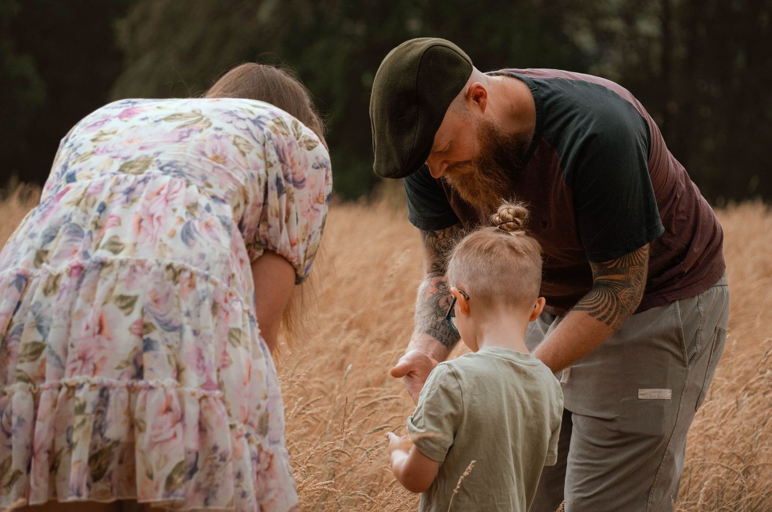 Parents bending down to interact with their young child in a golden wheat field during a family shoot.
