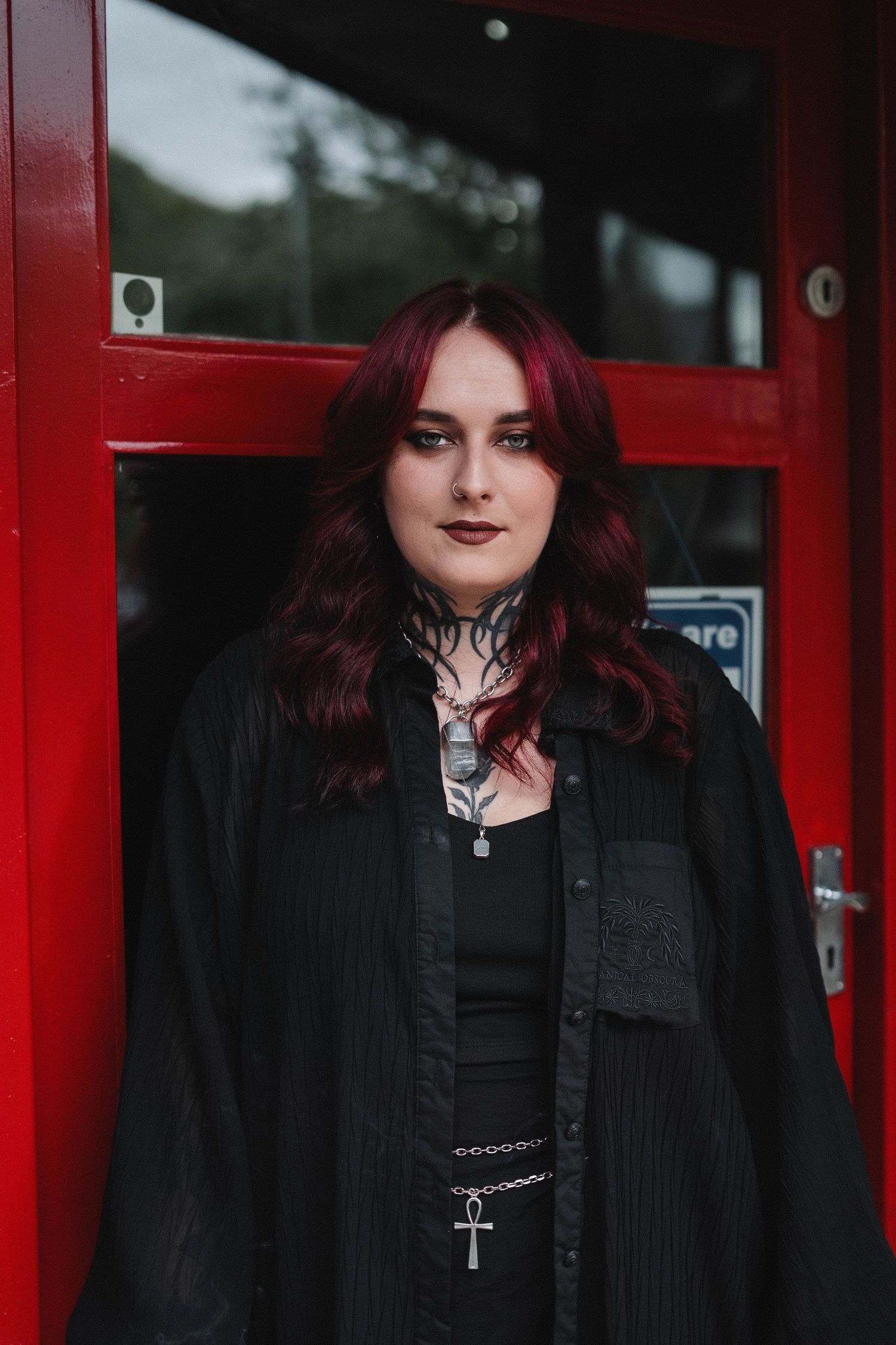 Young woman with dark red hair and gothic style standing in front of red doors.
