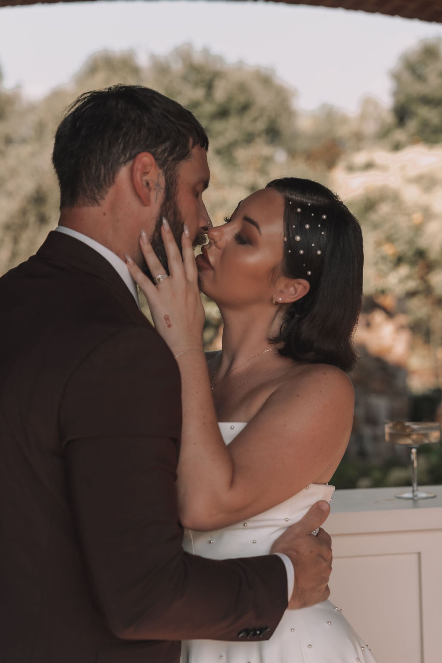 Bride and groom sharing a romantic kiss in wedding attire, bride wearing pearl hair accessories and white strapless gown.