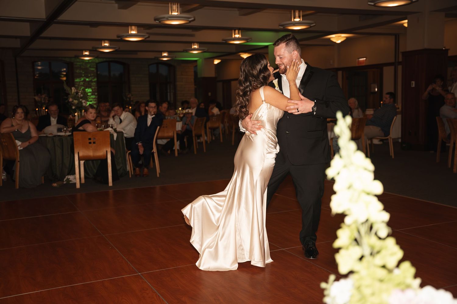 Couple sharing their first dance at wedding reception in elegant ballroom with guests seated at tables.