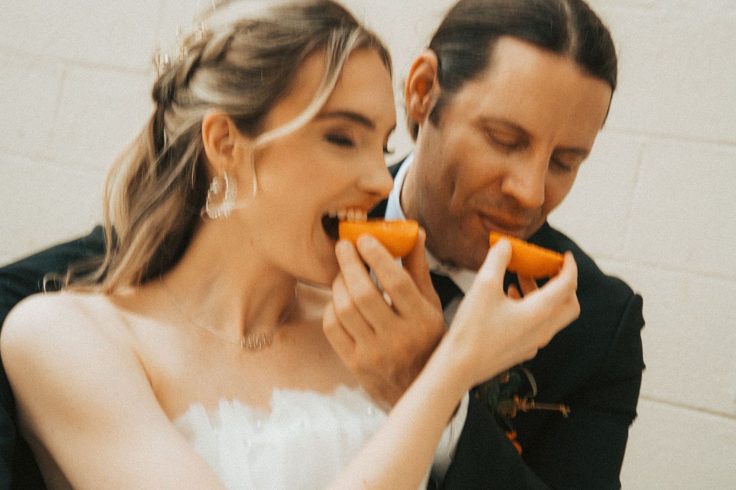 Bride and groom joyfully eating orange slices together on their wedding day in a candid fun moment.