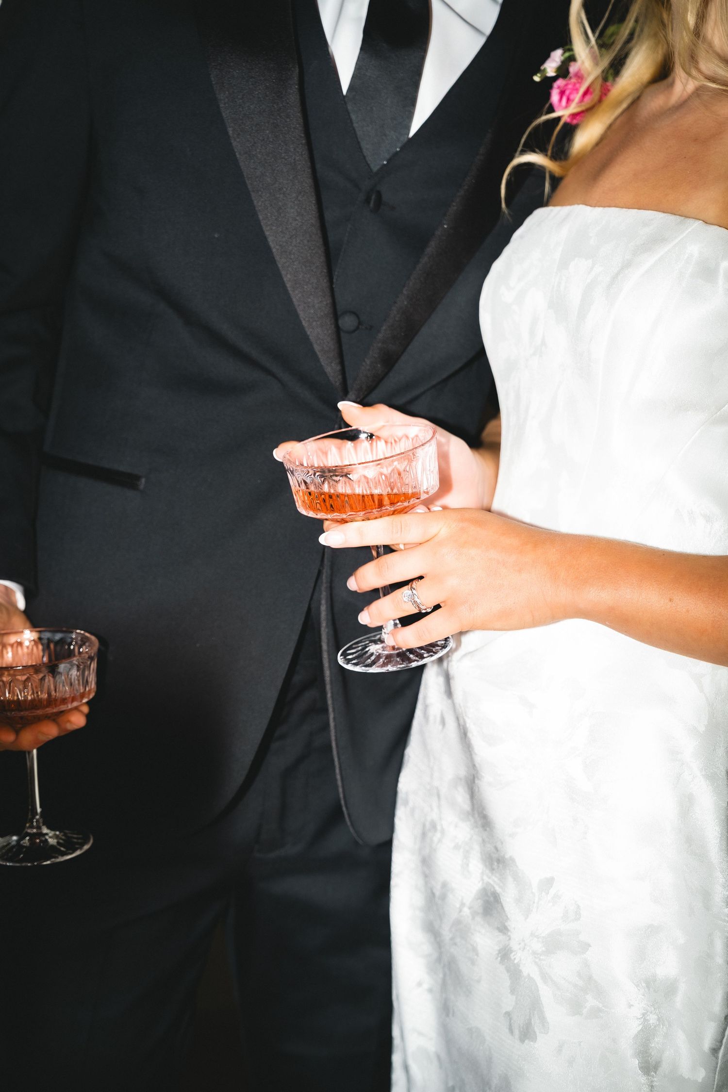Bride and groom holding cocktails at wedding reception, bride wearing white strapless gown with diamond ring.