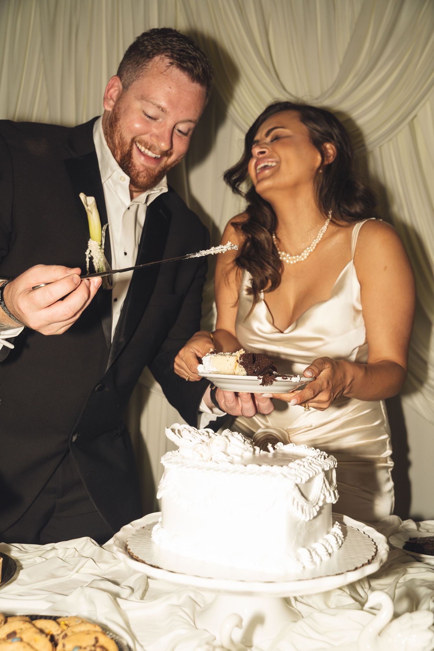 Smiling bride and groom cutting their white wedding cake together at their reception.
