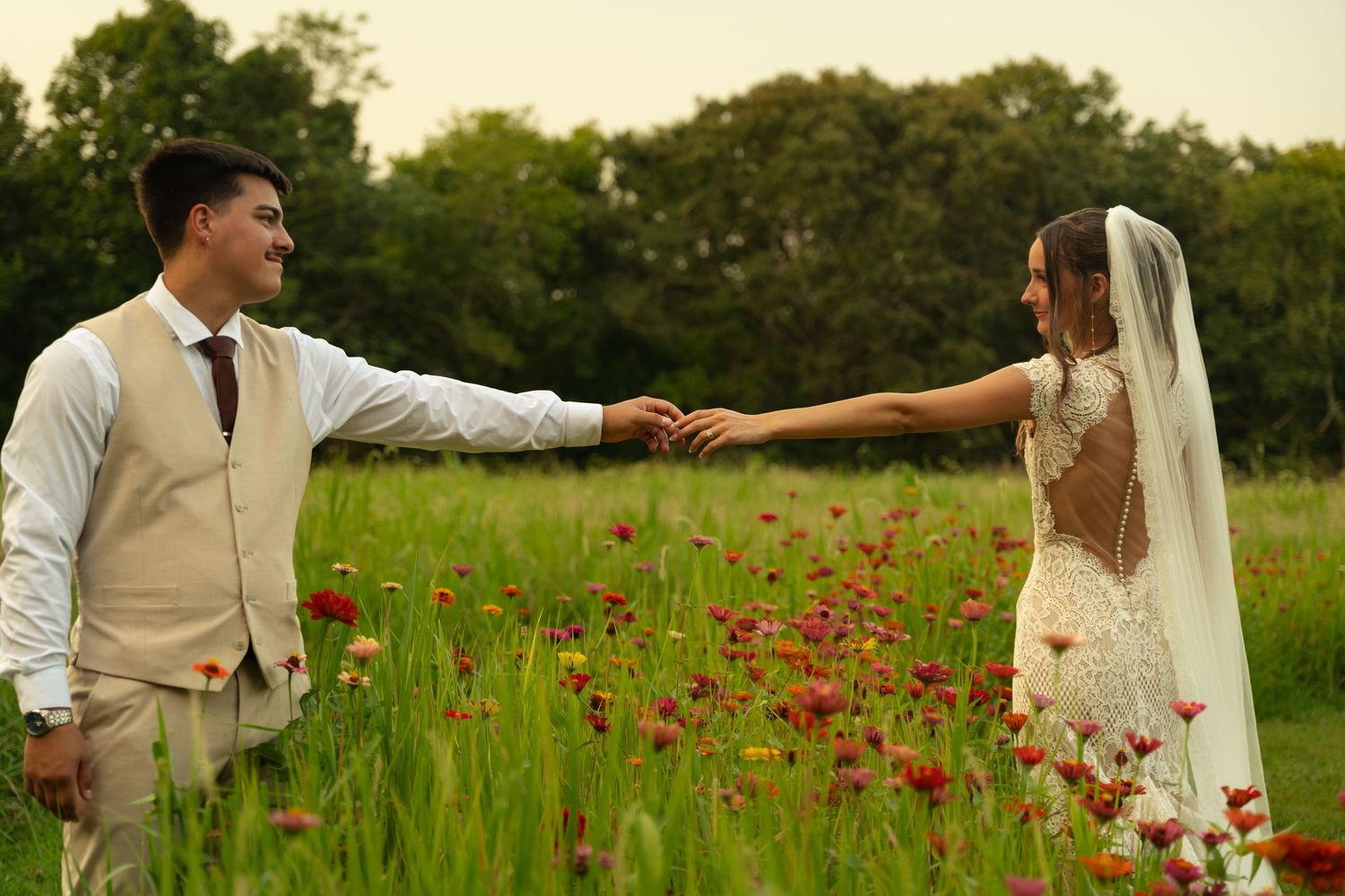 A bride and groom hold hands in a blooming wildflower meadow, sharing a romantic moment on their wedding day.