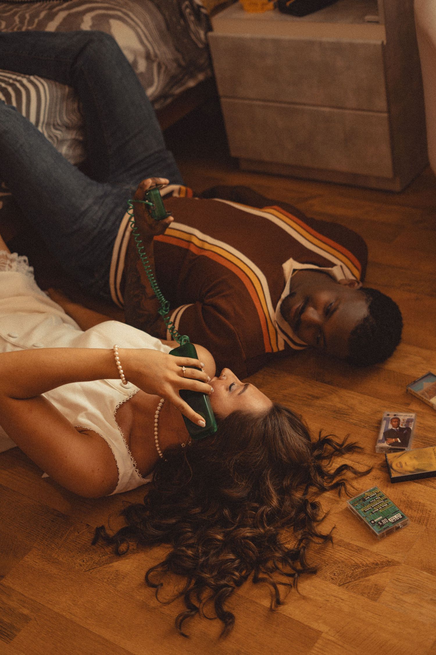 Couple lying on a wooden floor laughing together while holding a vintage green telephone.