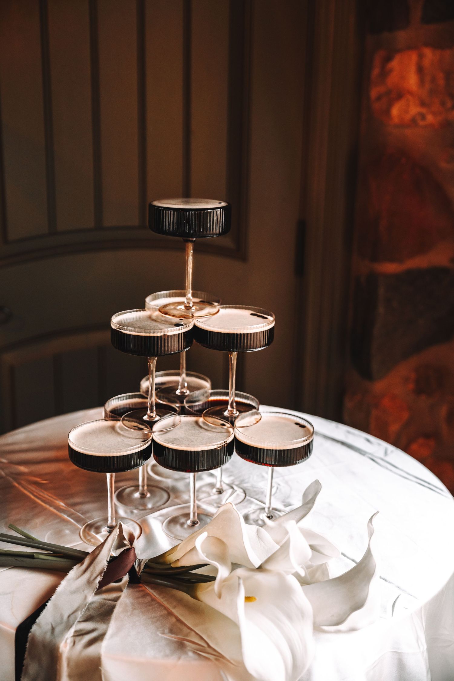 Elegant champagne glass tower pyramid arranged on a white tablecloth with white flowers at a formal wedding reception.