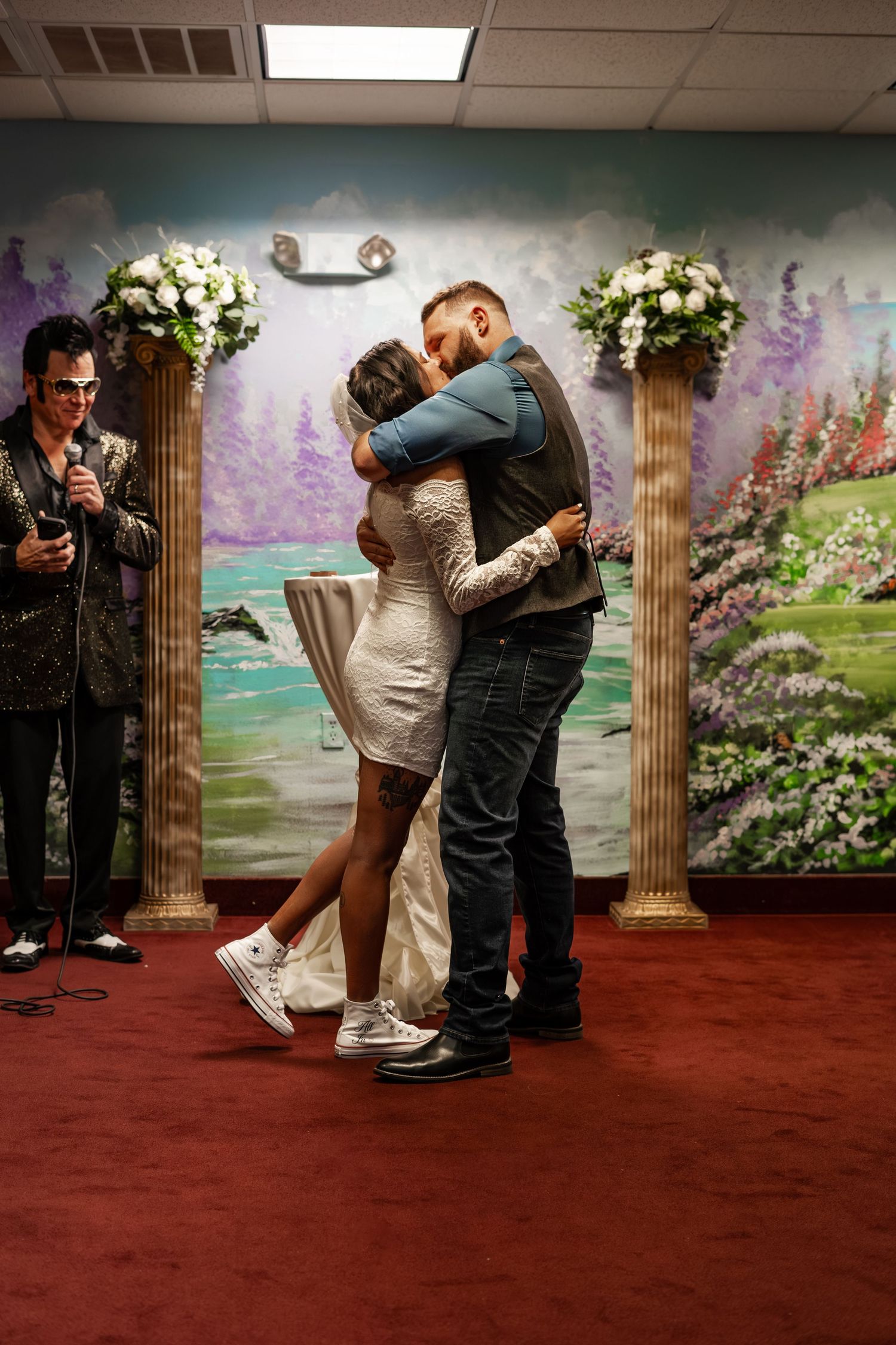 Couple shares first kiss at Las Vegas wedding chapel with officiant and floral columns in background.