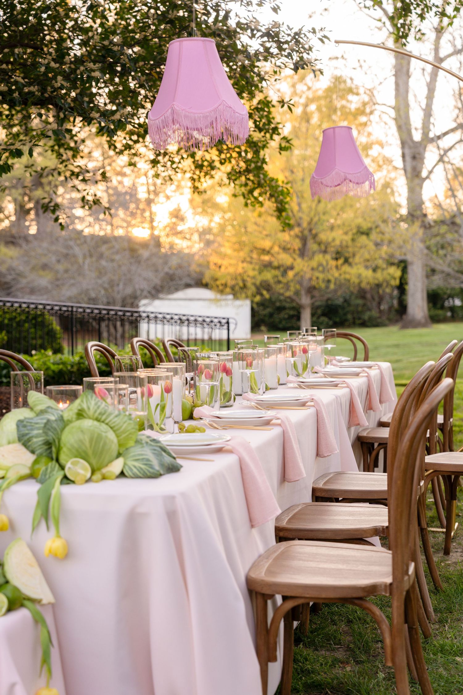 Elegant outdoor wedding reception table with pink linens, pink fringe lampshades, and floral centerpieces.