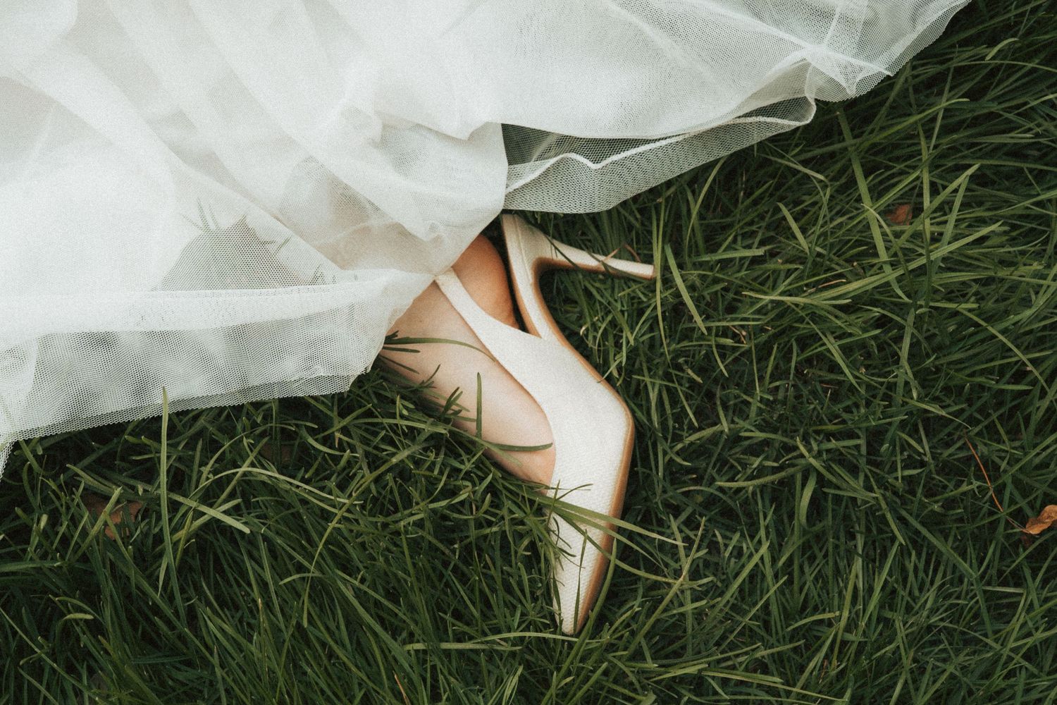 Bridal heels on green grass beneath a white wedding gown.