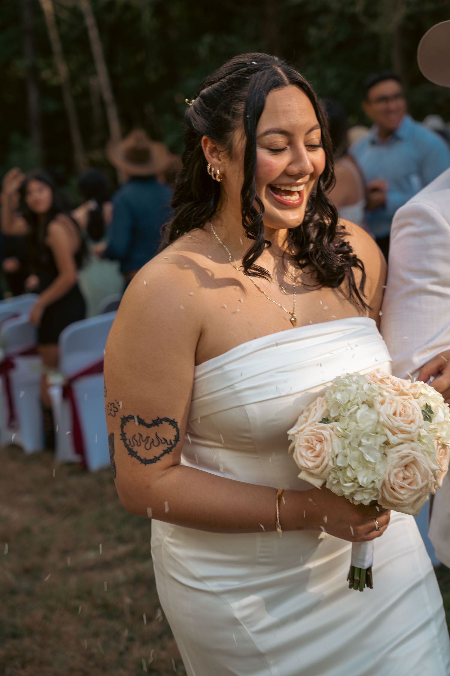 Joyful bride in strapless gown holding white rose bouquet.