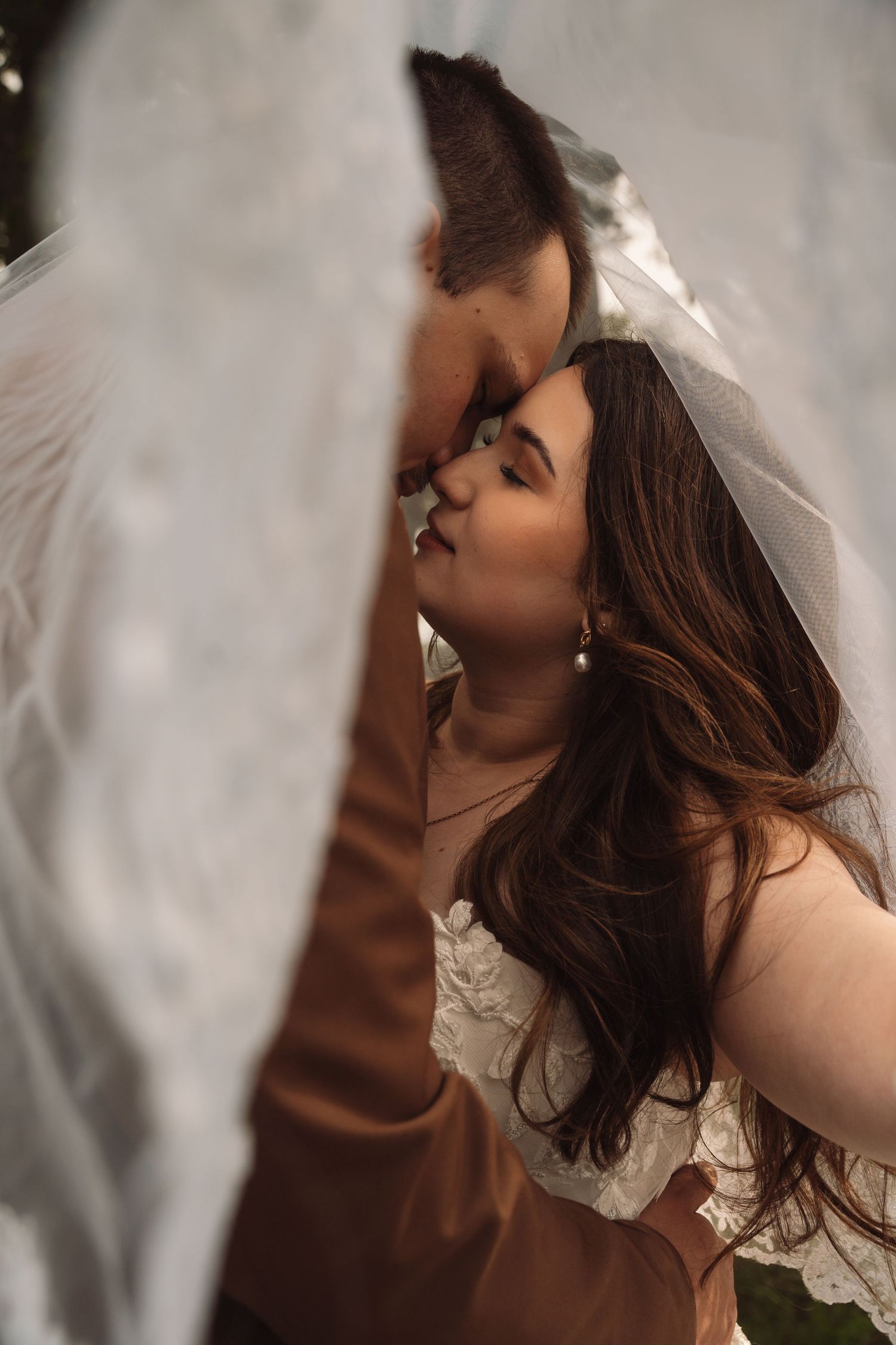 Bride and groom sharing a romantic kiss under a flowing white wedding veil on their wedding day.