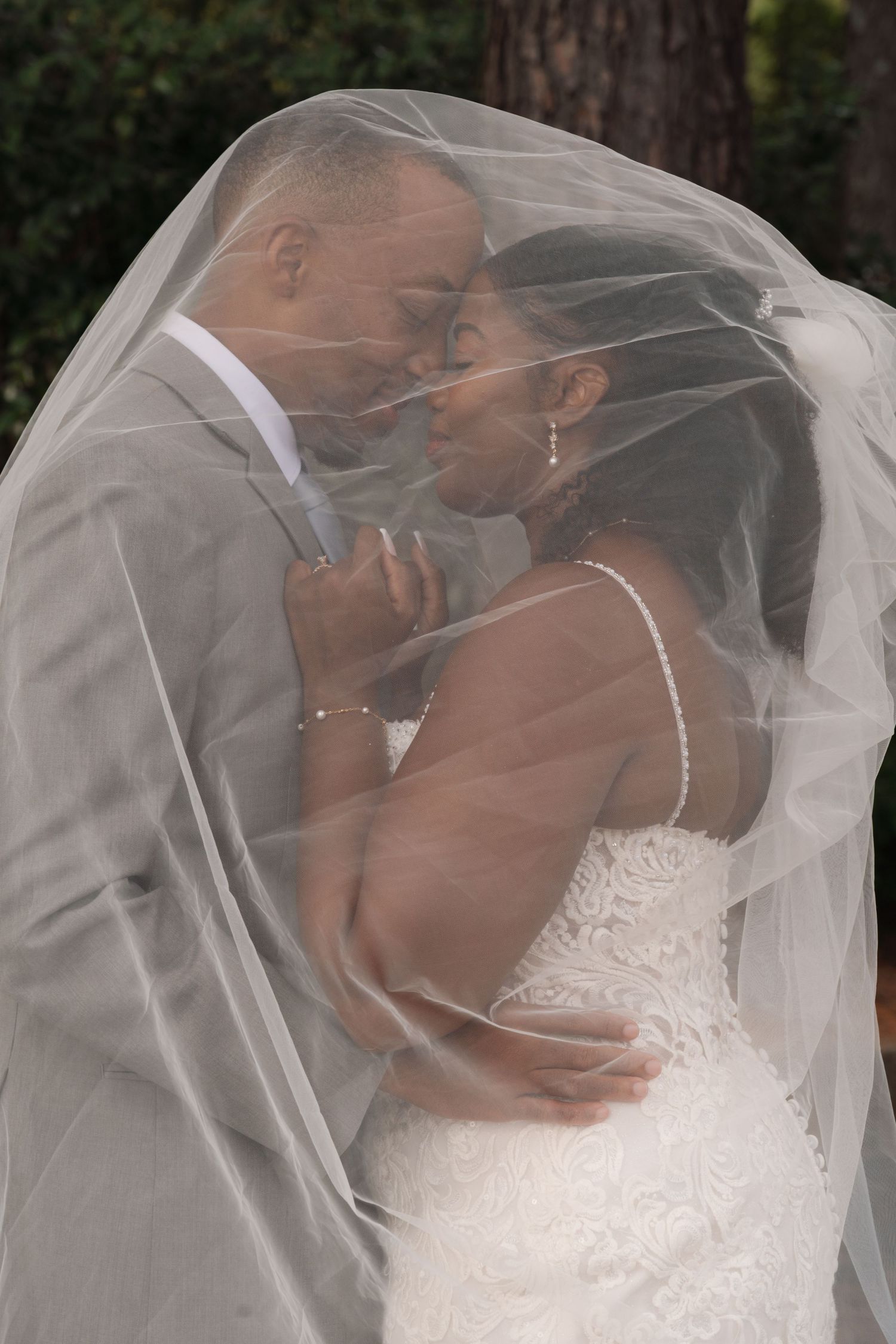Bride and groom share a romantic kiss under a flowing white veil on their wedding day.