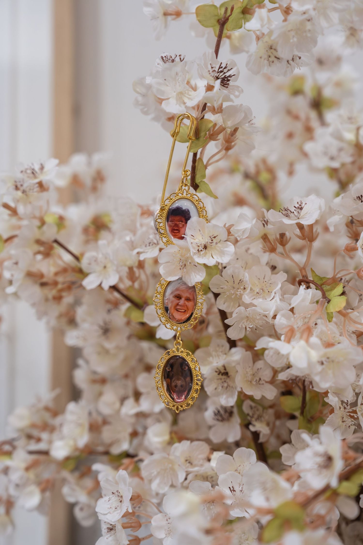 Gold oval lockets with miniature portraits hang from a blooming cherry blossom branch with white flowers.
