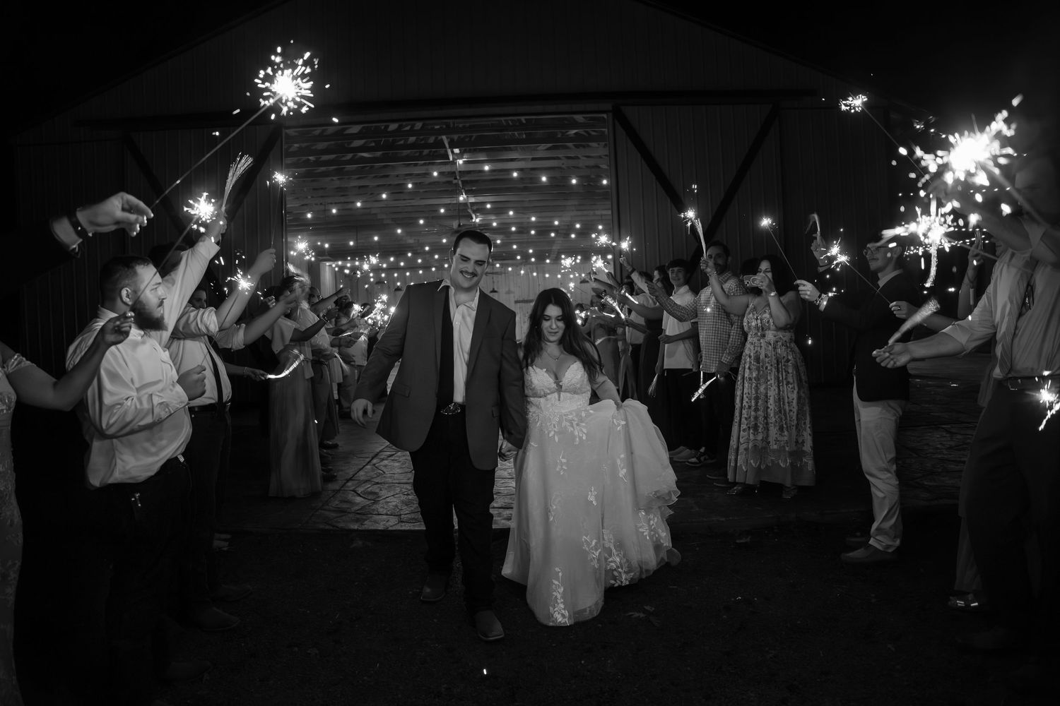 Black and white photo of bride and groom walking through sparkler tunnel at night wedding reception.