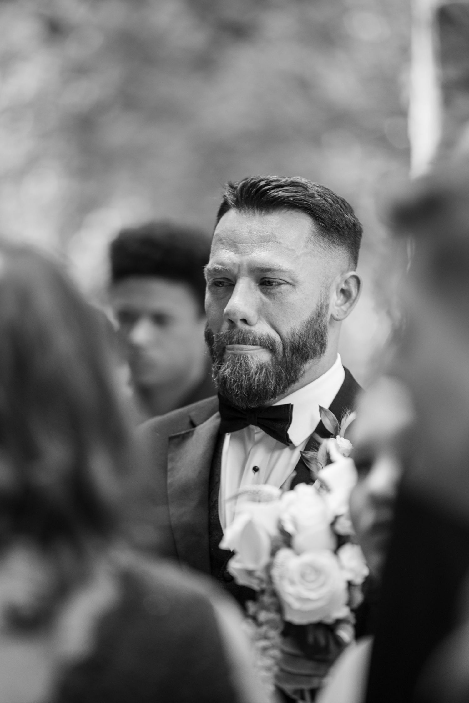 Emotional groom in tuxedo with bow tie and boutonniere, black and white wedding ceremony portrait.