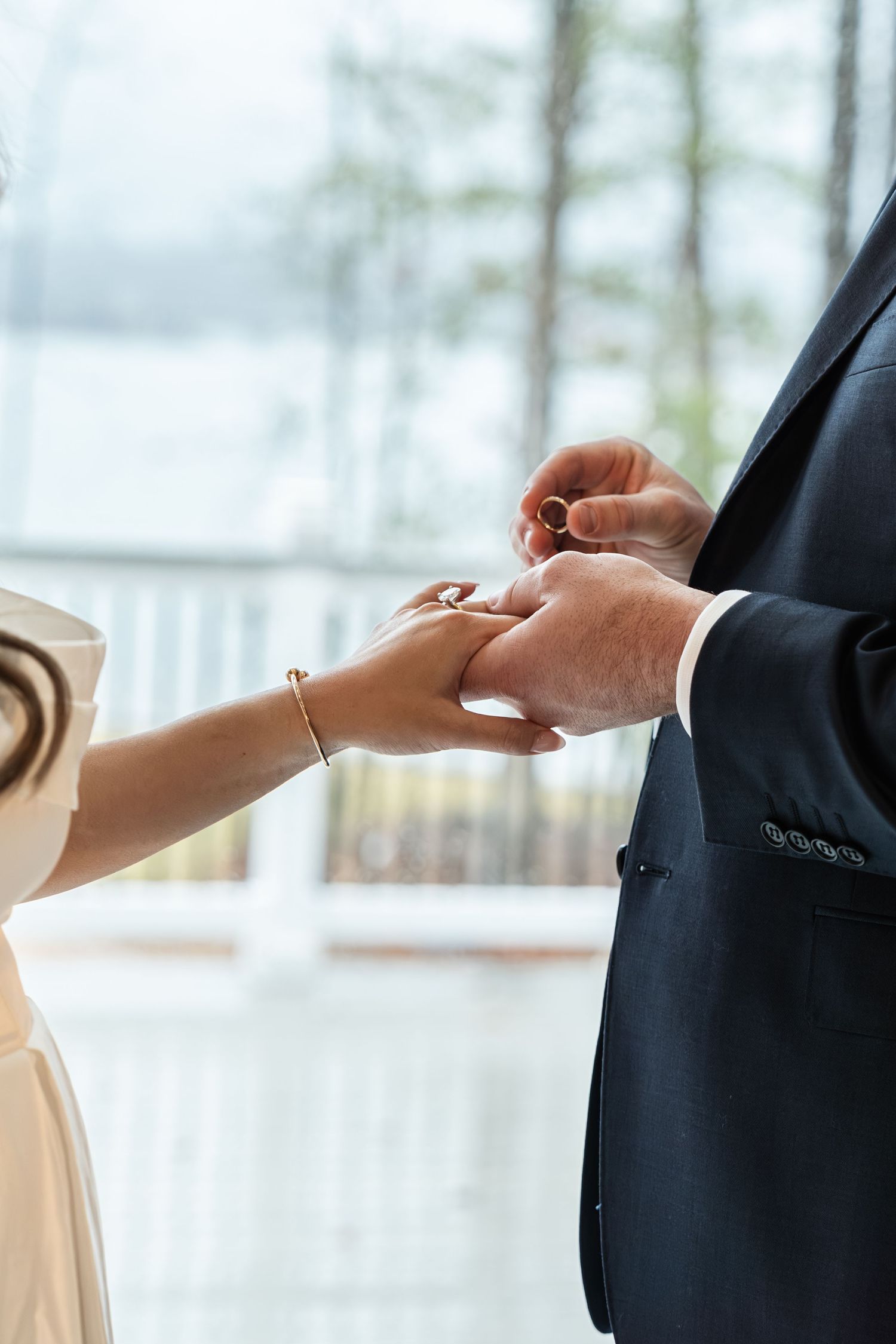 Groom placing wedding ring on brides finger during ceremony near window.