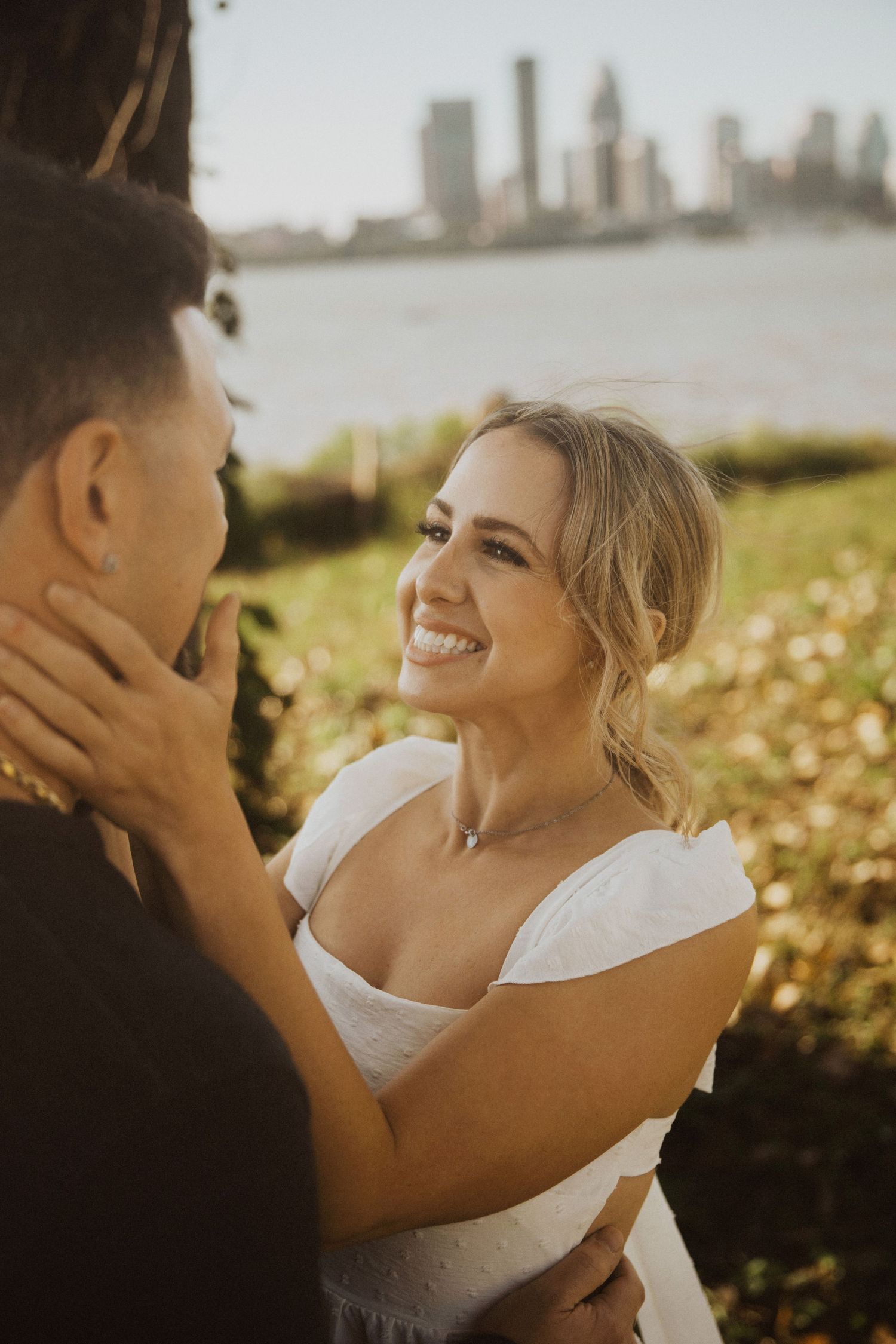 Couple sharing joyful laughter during sunset with city skyline in background.