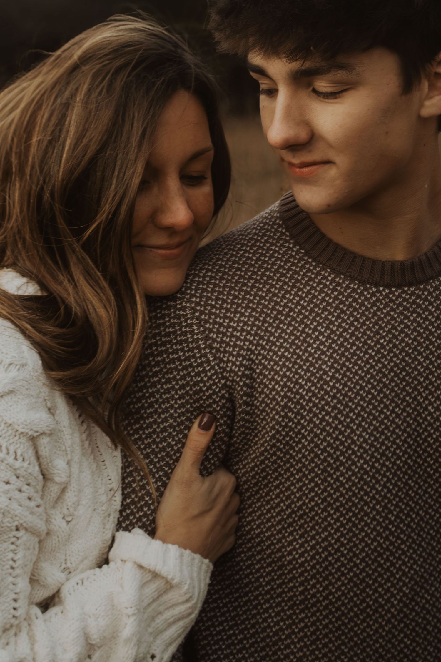 A young couple in cozy knit sweaters share a tender moment, with the woman leaning her head on the man's shoulder.