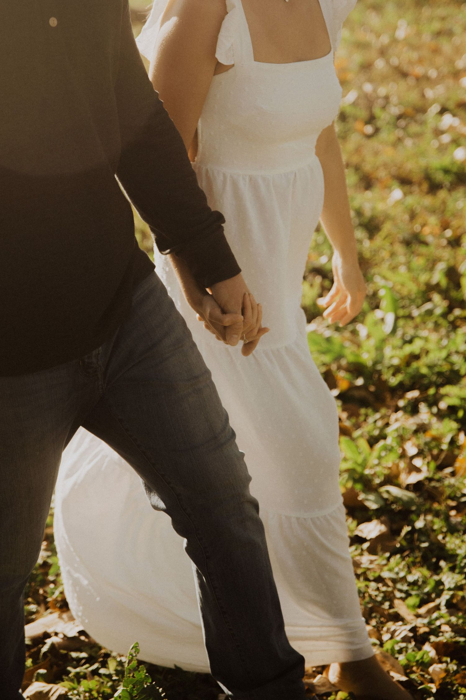 Couple in white and black attire walking together through sunlit garden.