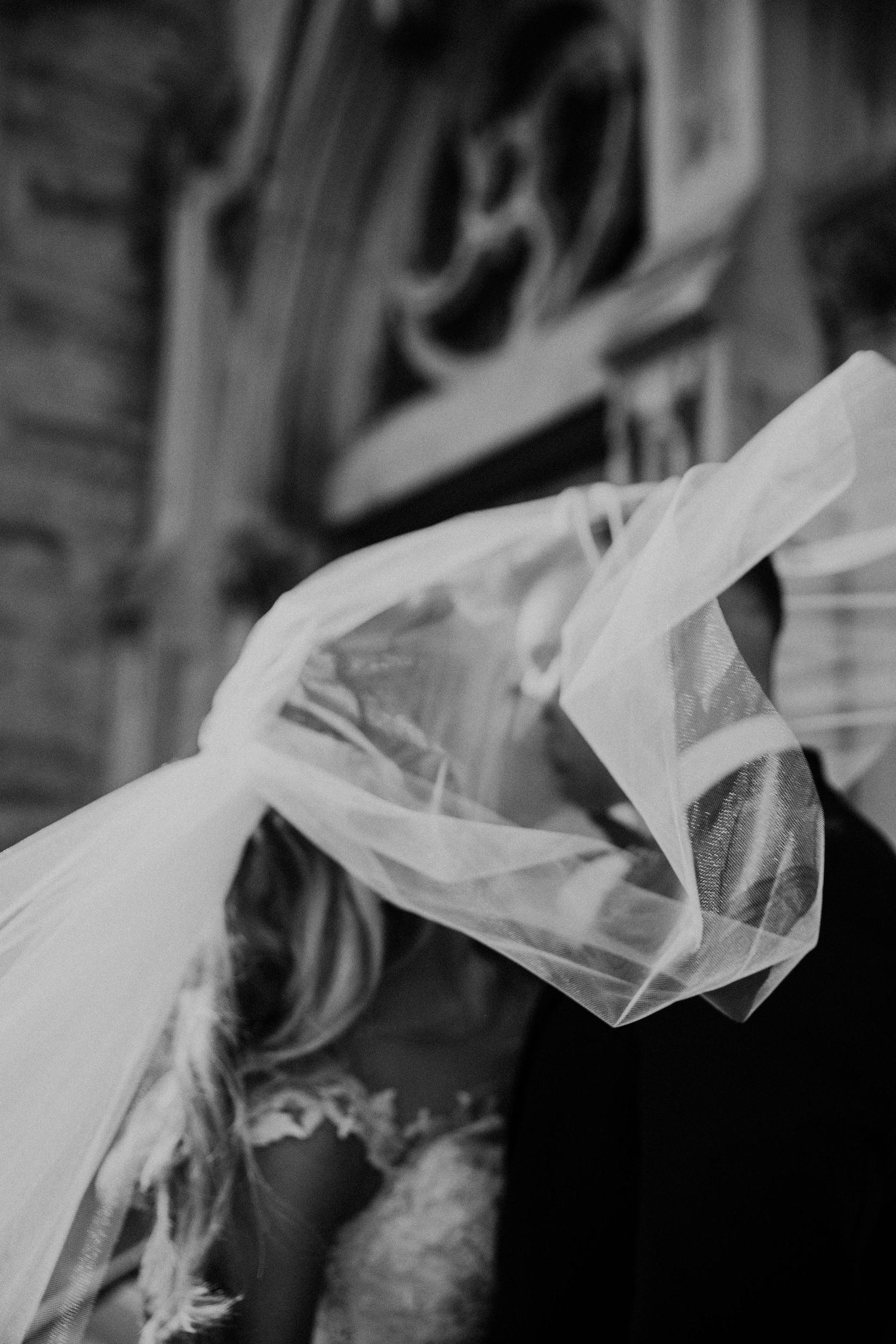 Artistic black and white detail of wedding veil flowing in breeze during intimate moment.