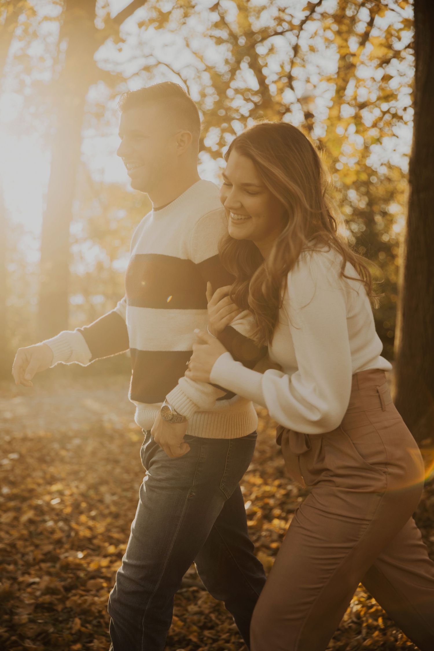 A couple embracing and laughing together in a sunlit autumn forest.