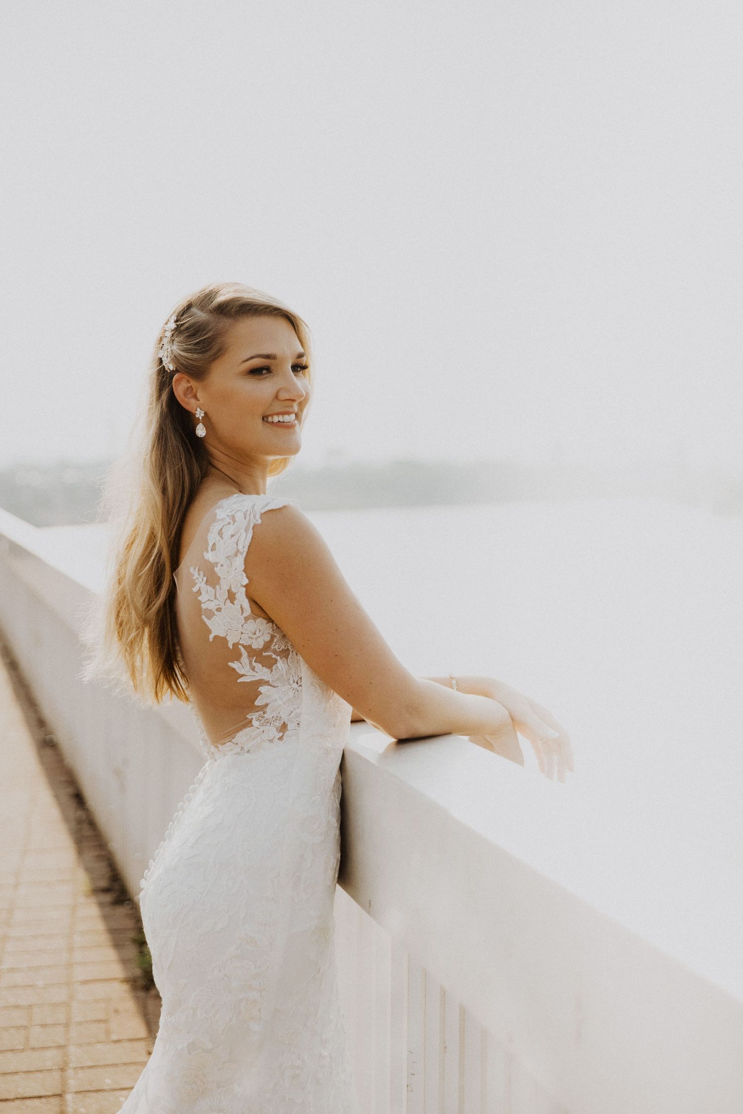 Bride in a lace wedding dress poses against a bright background, showing off the elegant back detail.