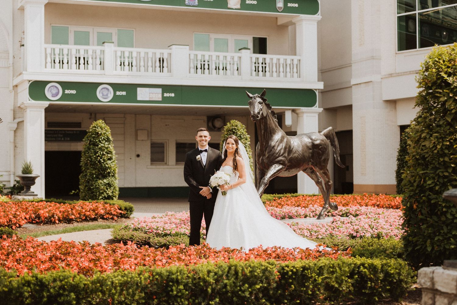 Wedding party poses in front of a grand building with colorful flower gardens.