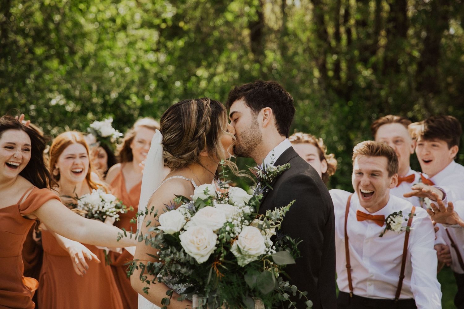 Wedding party celebrates with joyful expressions in a sunlit garden setting.
