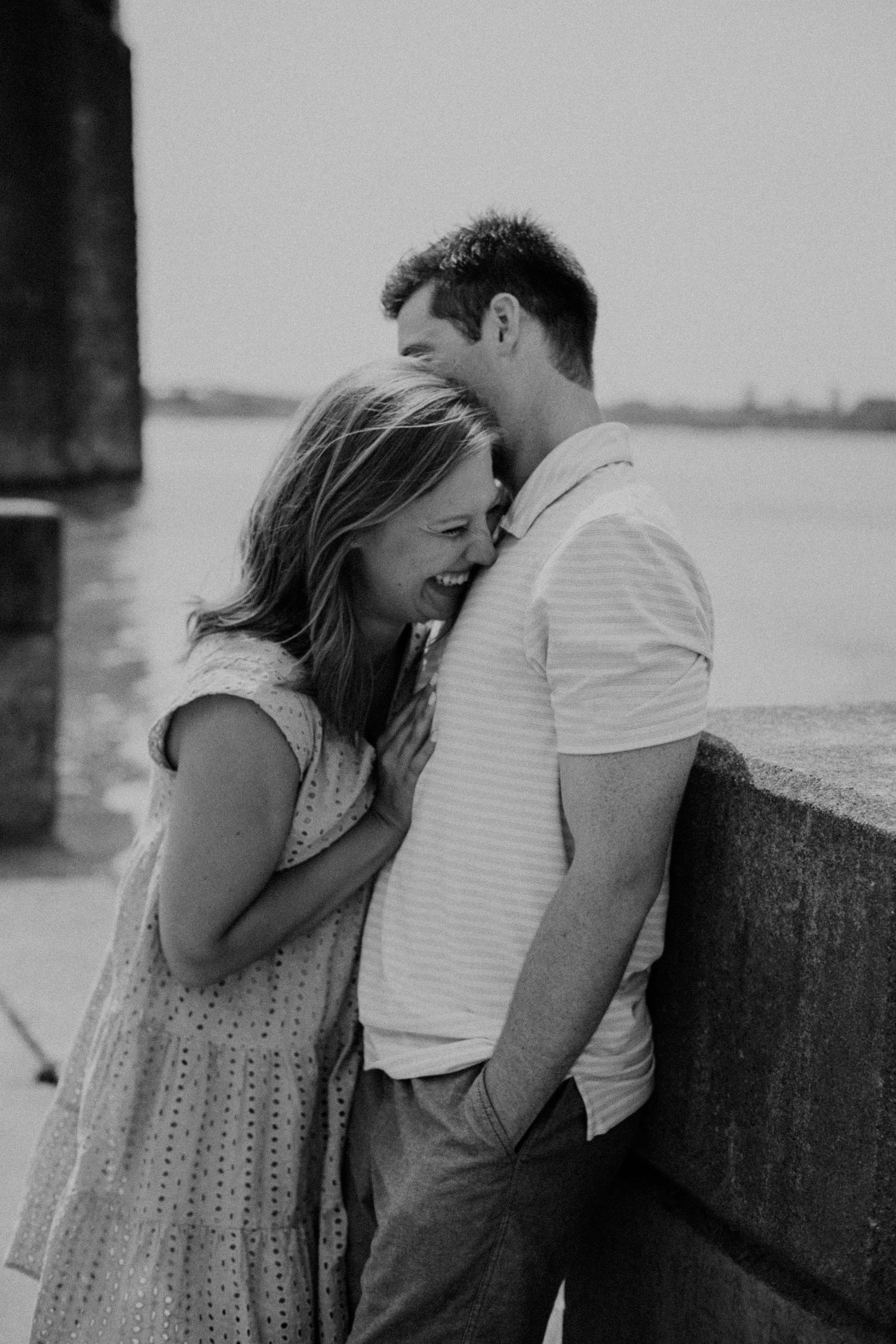 Couple shares playful moment against concrete wall in black and white photo.
