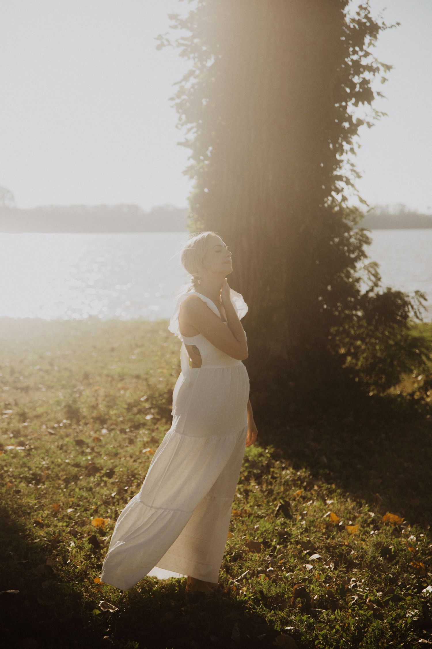 Bride in white dress twirls gracefully in sunlit field during sunset.