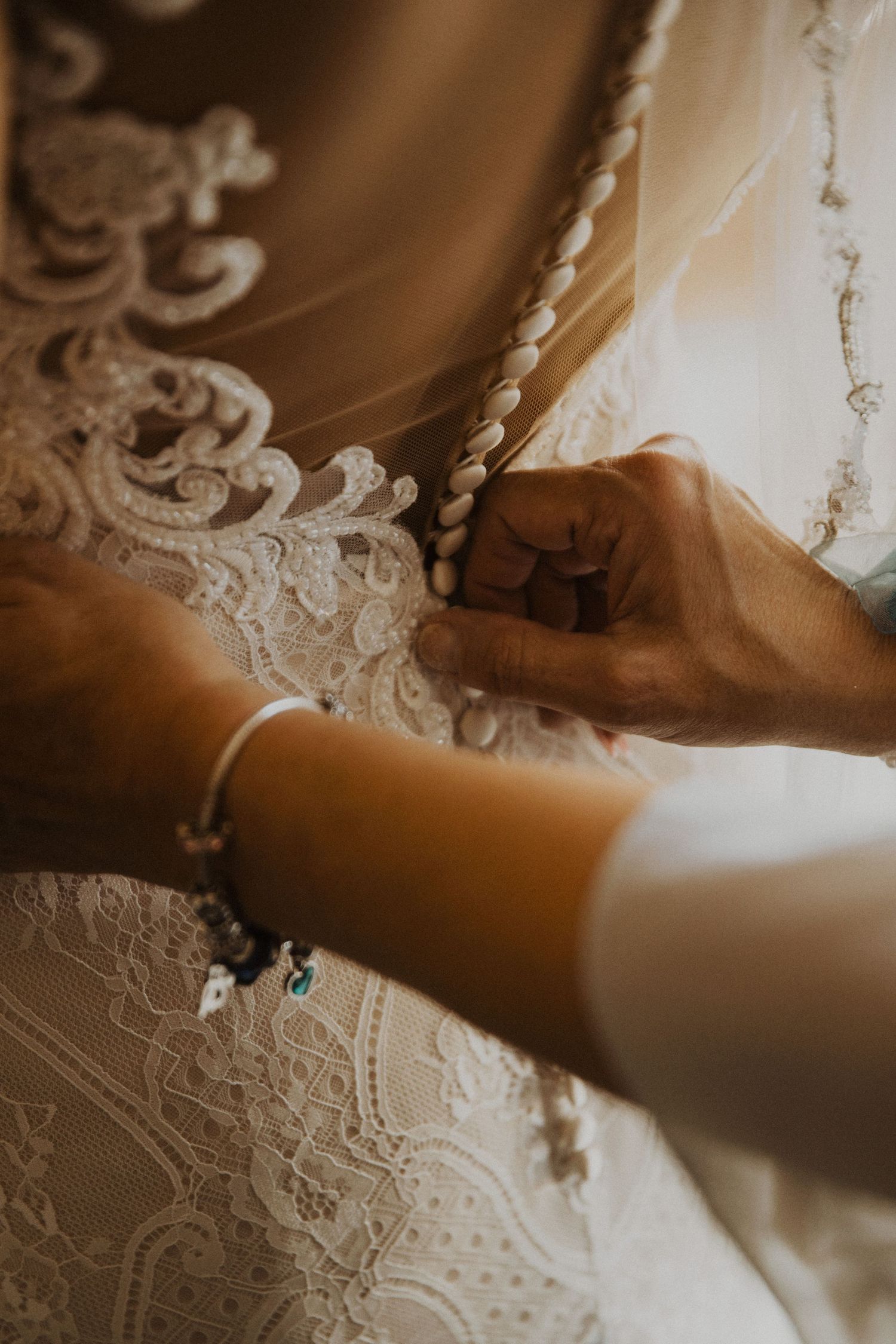 Detail shot of hands adjusting delicate lace on wedding dress.