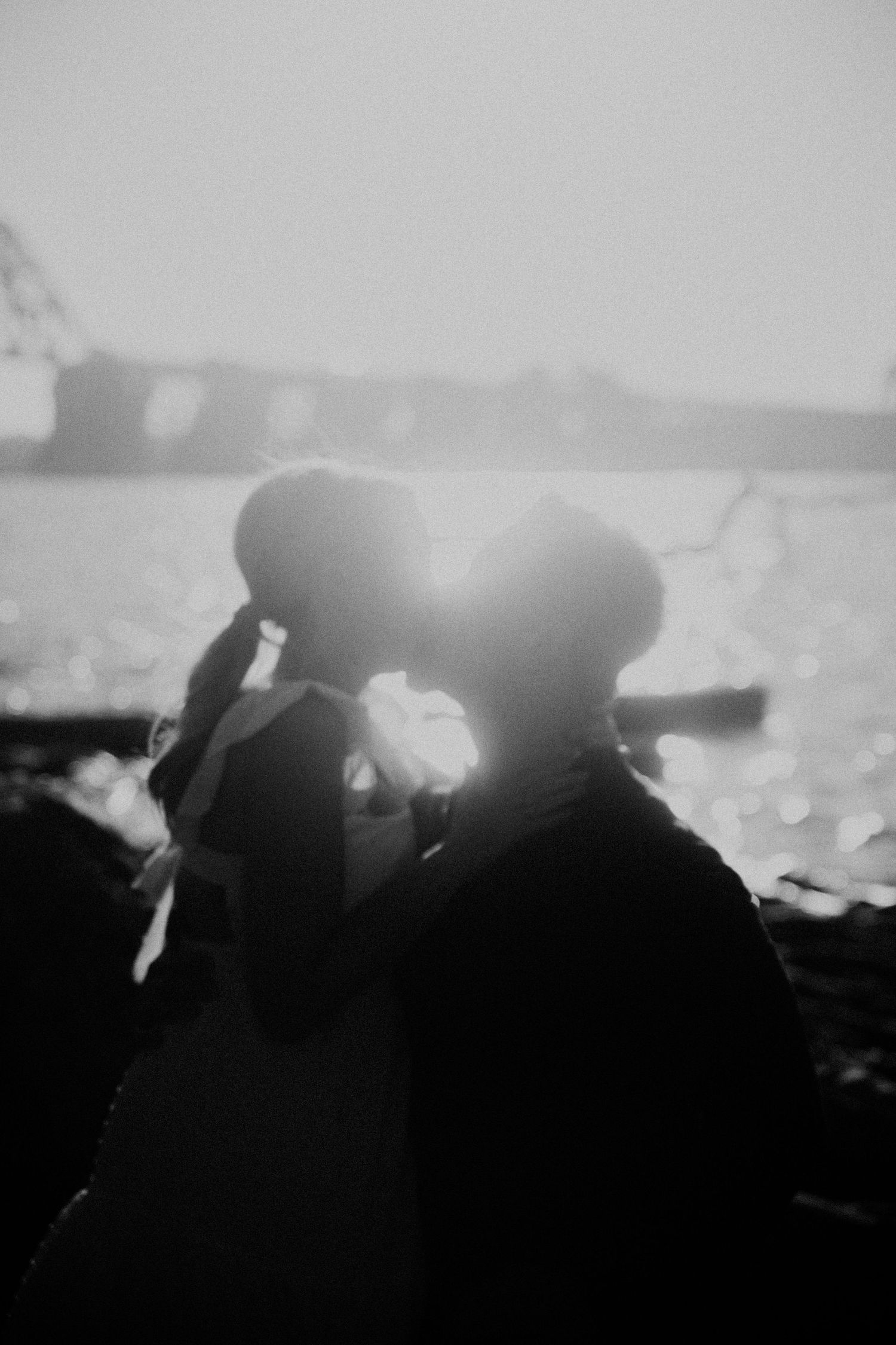 Silhouetted couple embraces against bright backlit sky.