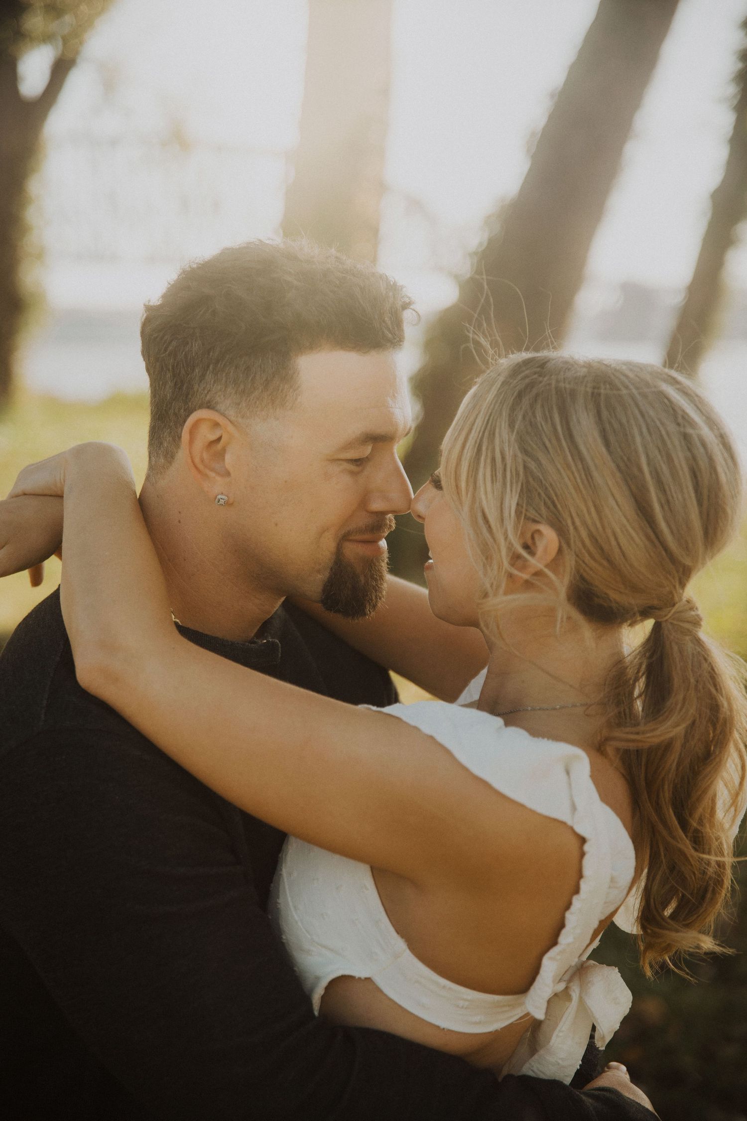 Romantic couple embraces in golden sunlight during outdoor photo session.