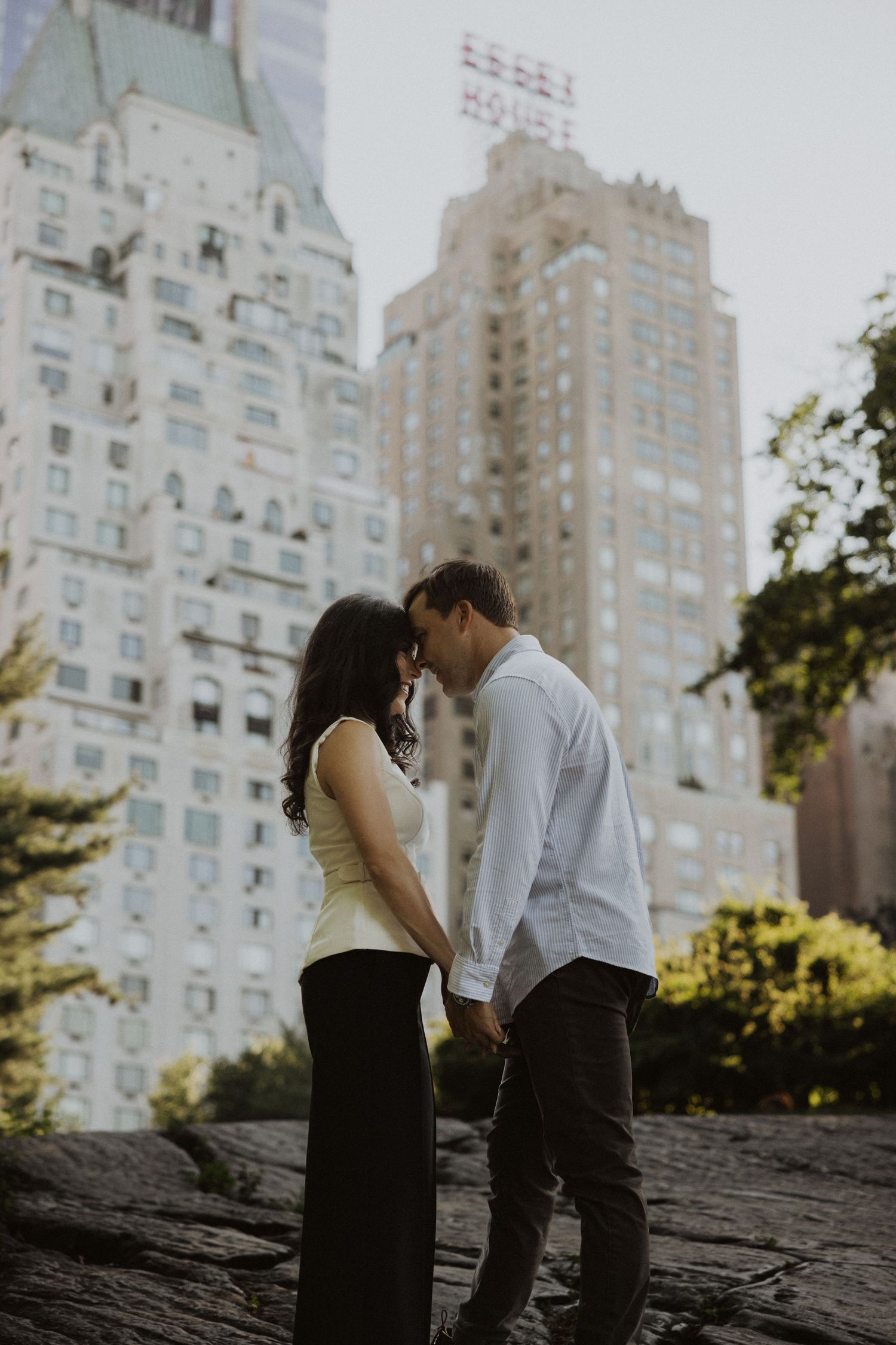 A couple shares a romantic moment in Central Park with NYC skyscrapers in the background.