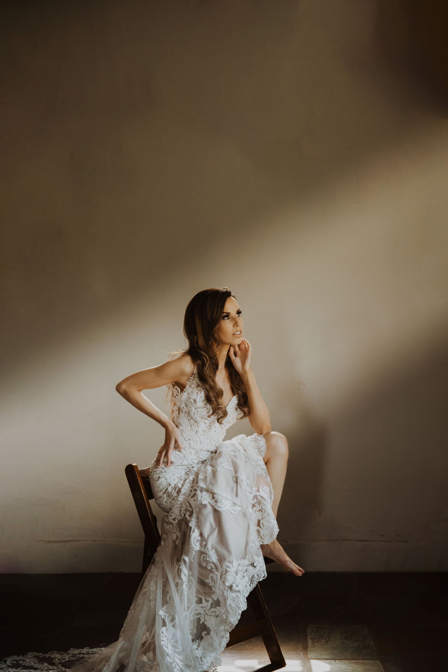 Artistic bridal portrait showing flowing white lace wedding dress in moody lighting.