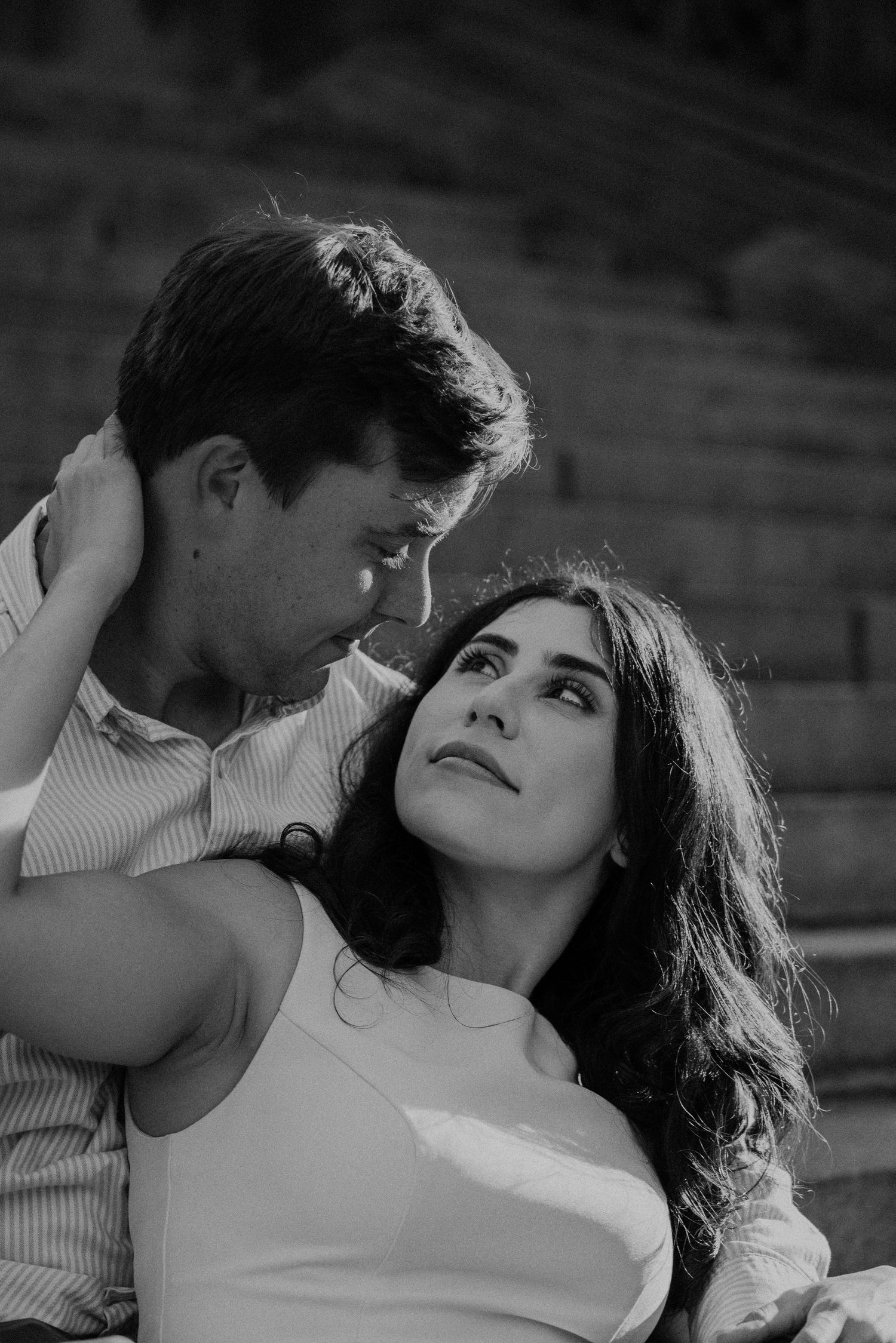 Black and white photo of a romantic couple gazing at each other tenderly outdoors on stone steps.