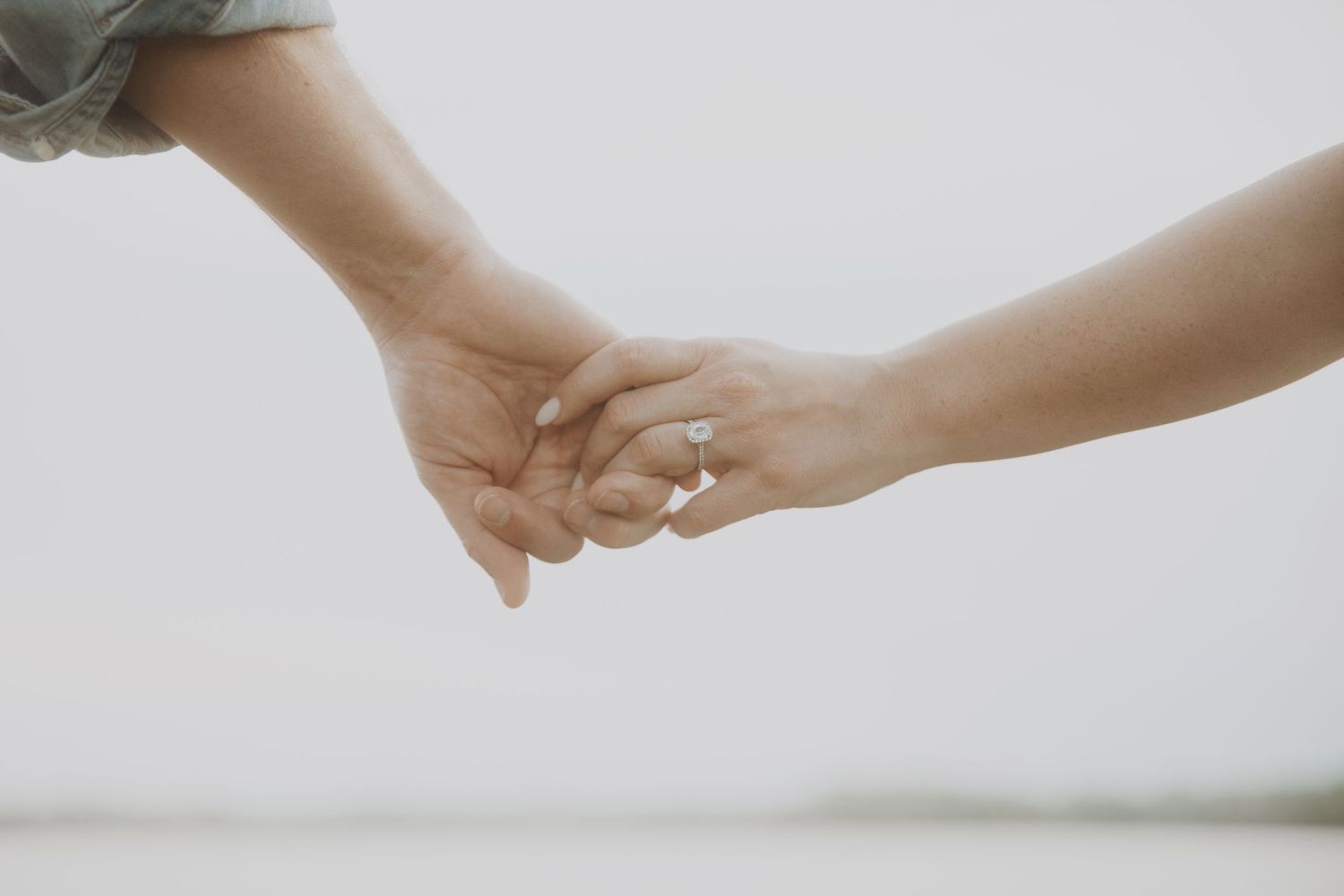 Close-up of hands reaching towards each other against a light background.