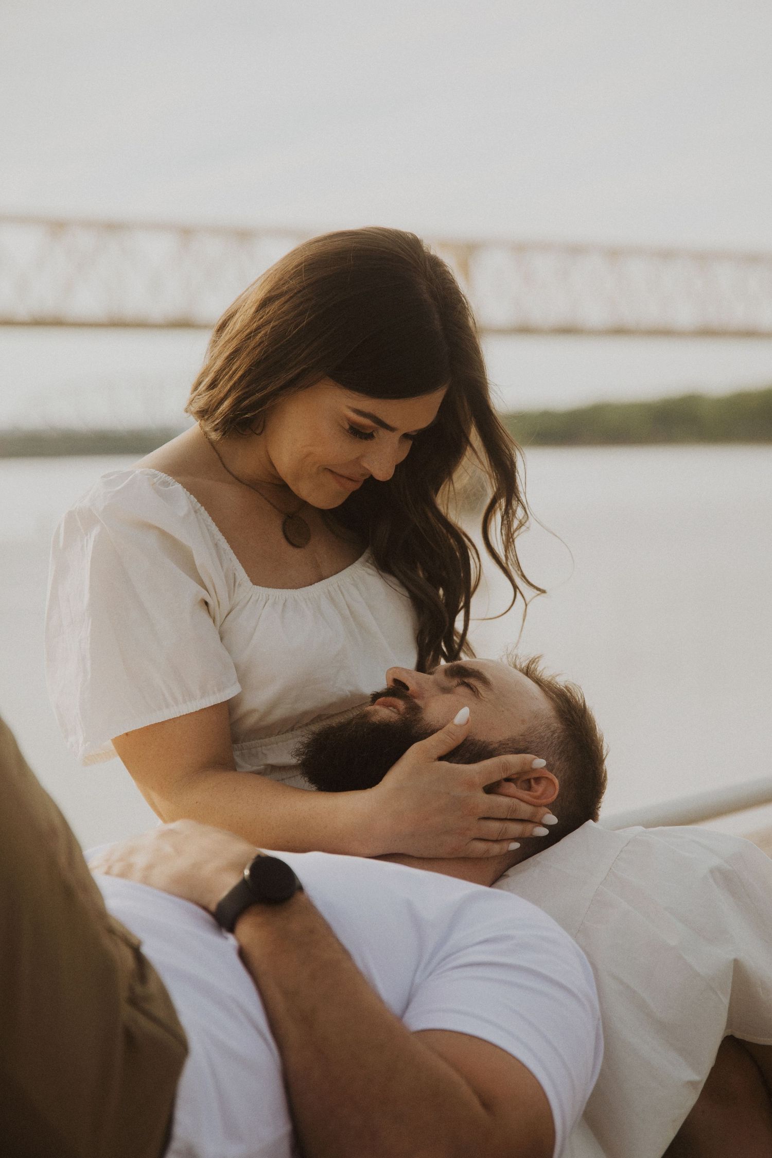 Intimate couple sharing tender moments together on white bedding in soft natural light.