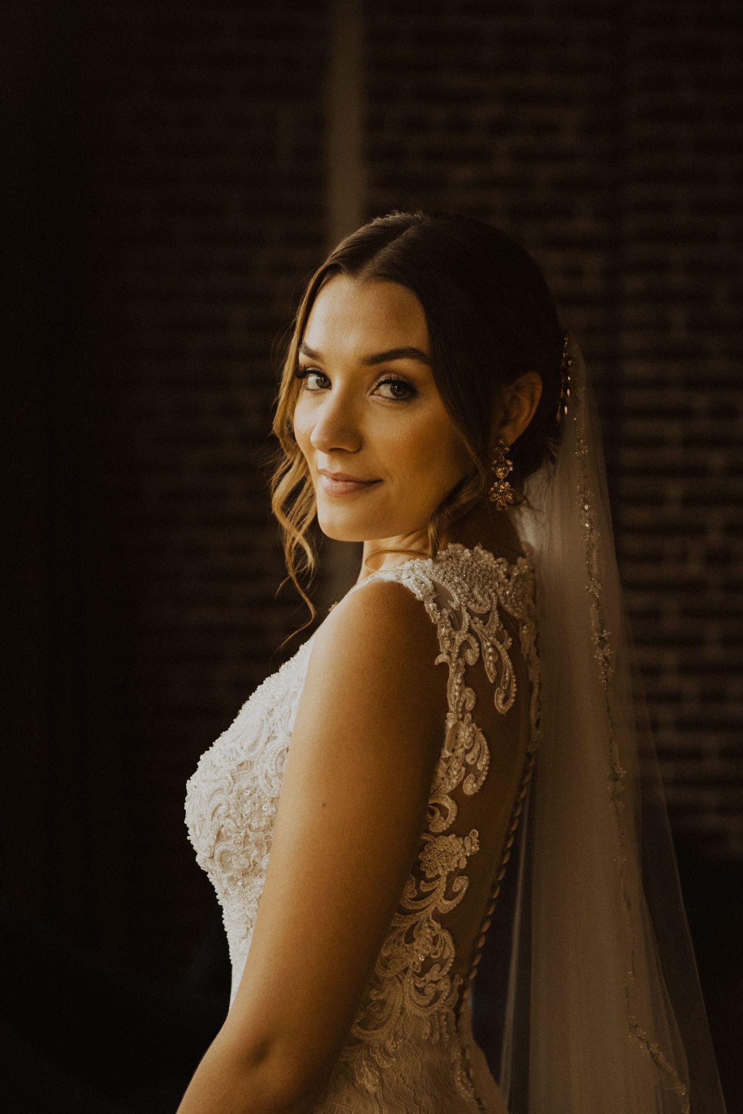 Dramatic bridal portrait showcasing detailed lace veil and wedding dress against dark background.