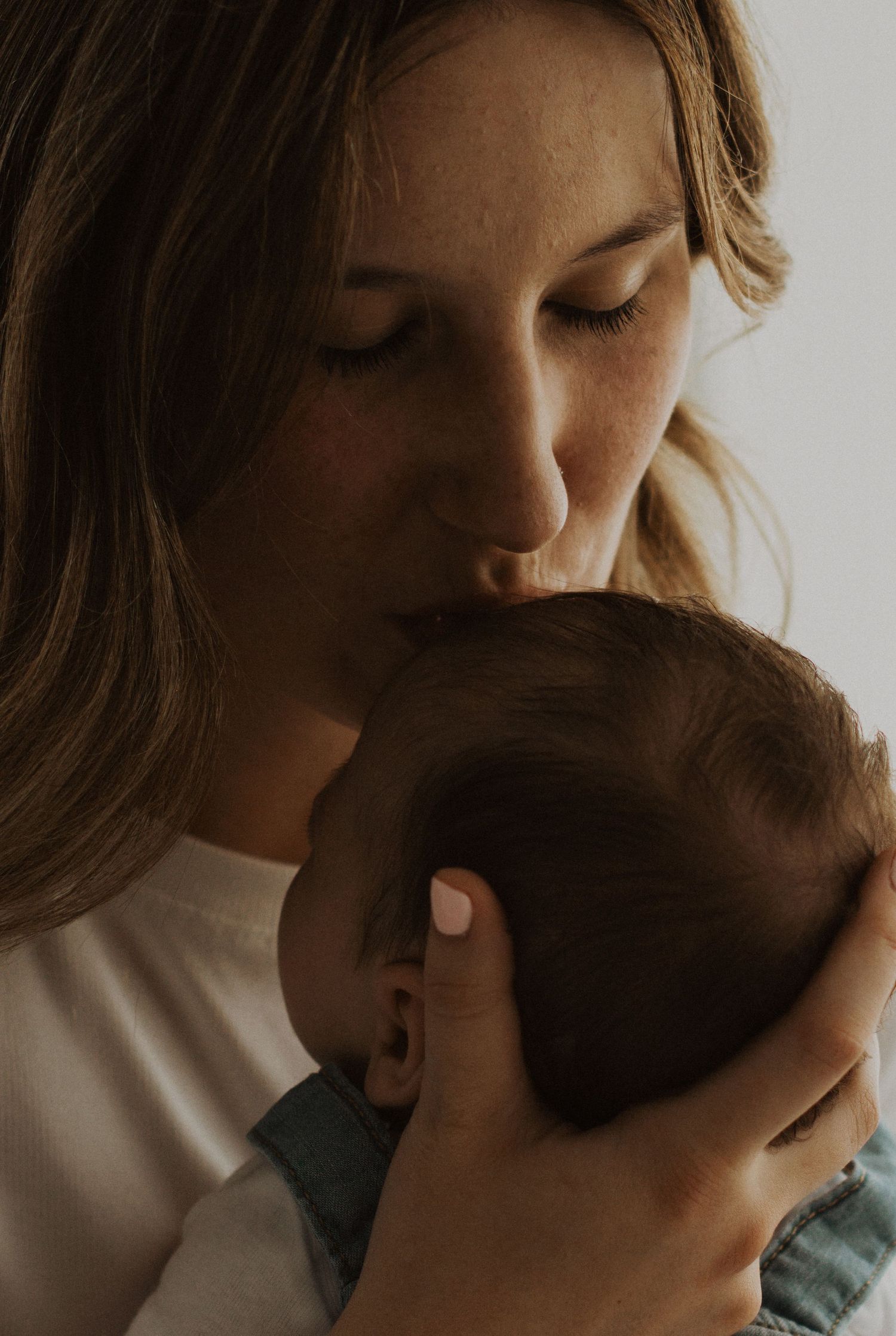 A tender moment as a young mother gently kisses her newborn baby's head while cradling it lovingly.
