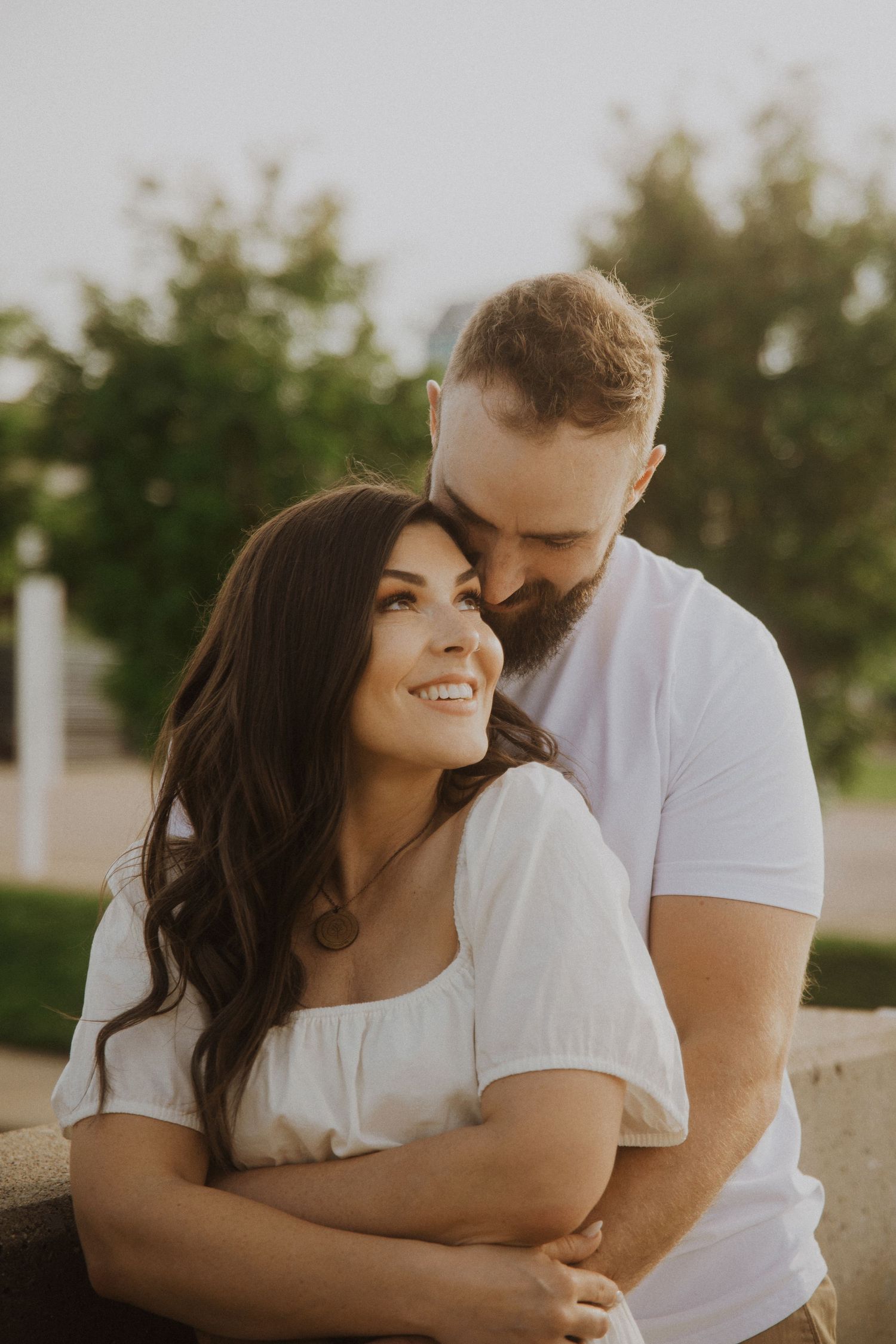 A couple laughs together during a sunset photoshoot against greenery.