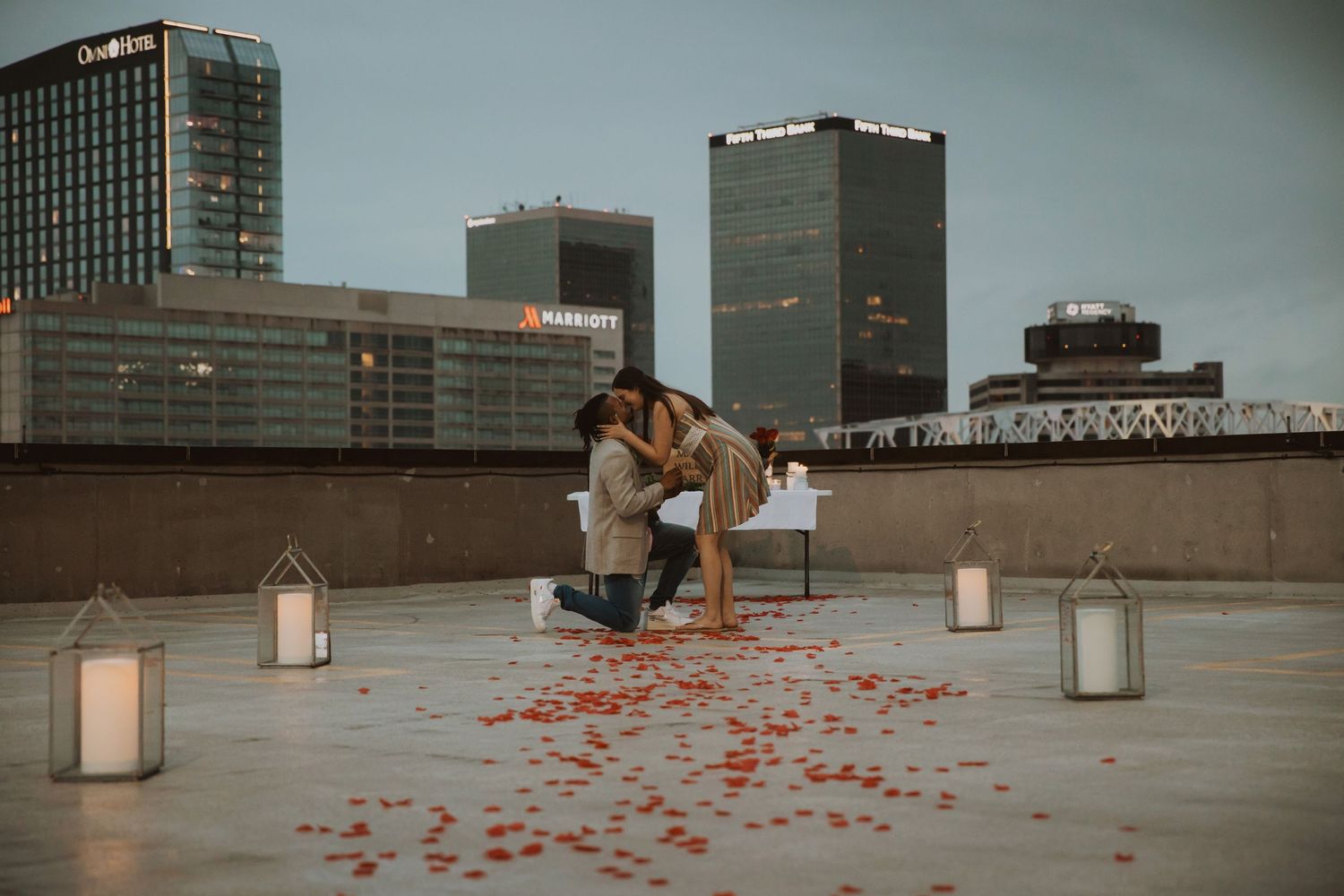 Urban rooftop decorated with romantic lanterns and rose petals against city skyline.