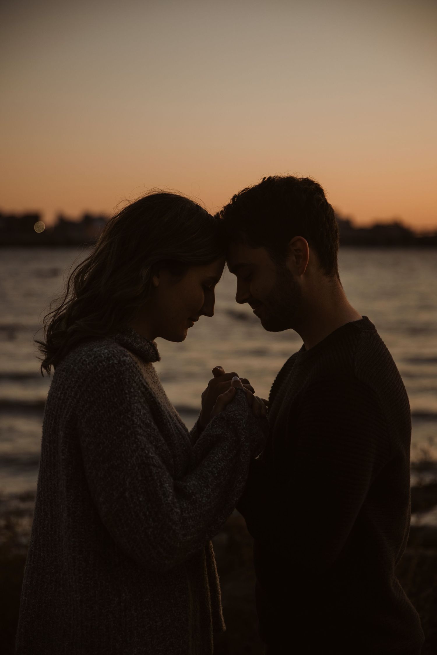 Silhouetted couple standing close together against sunset over water.