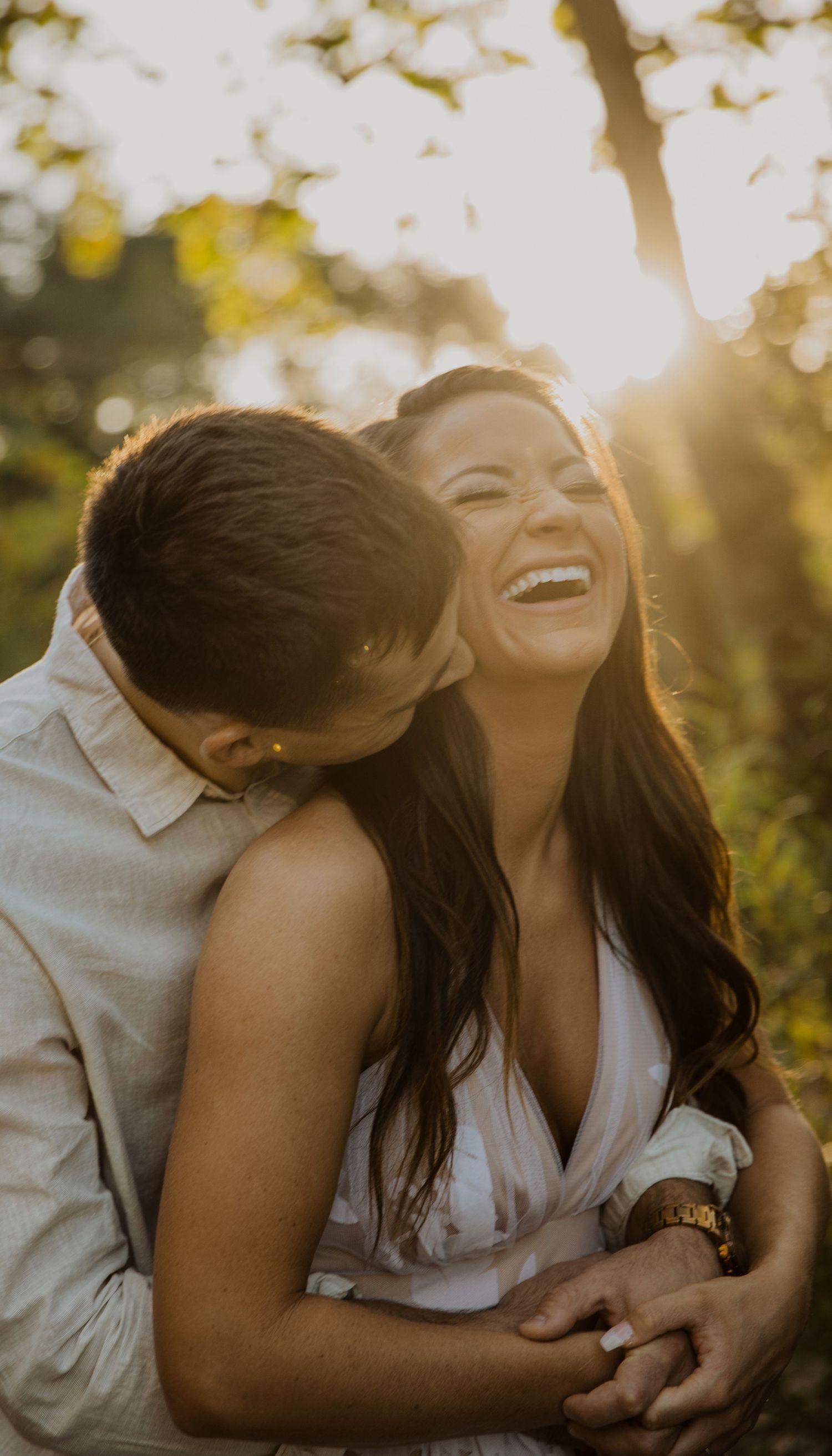 Two people share joyful laughter during a sunset photoshoot outdoors.