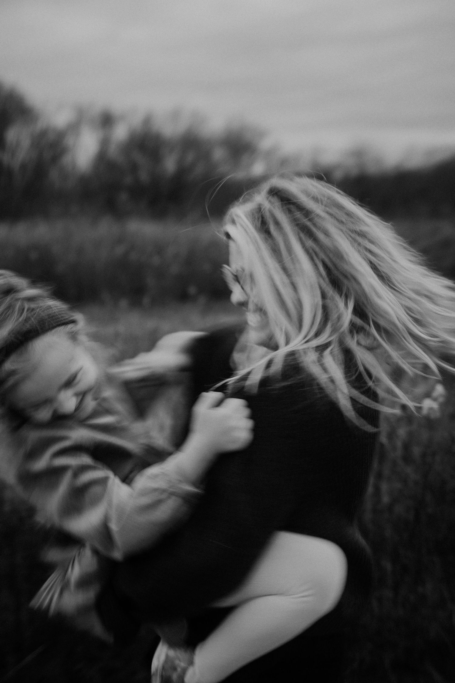 Black and white photo of a laughing woman spinning a young child outdoors in a field.