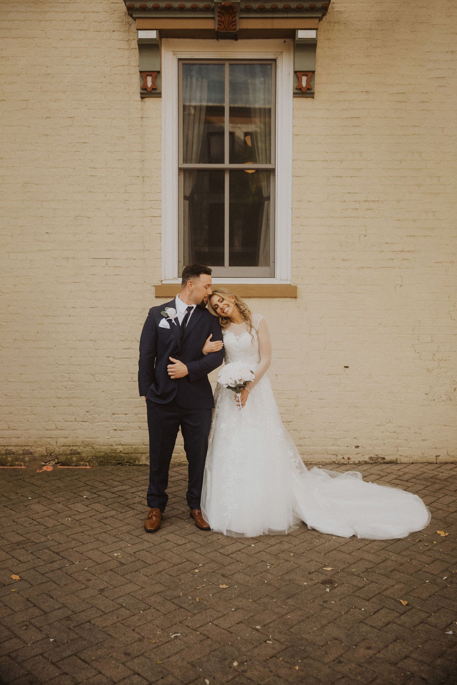 Wedding couple poses against cream brick wall with classic architectural details.