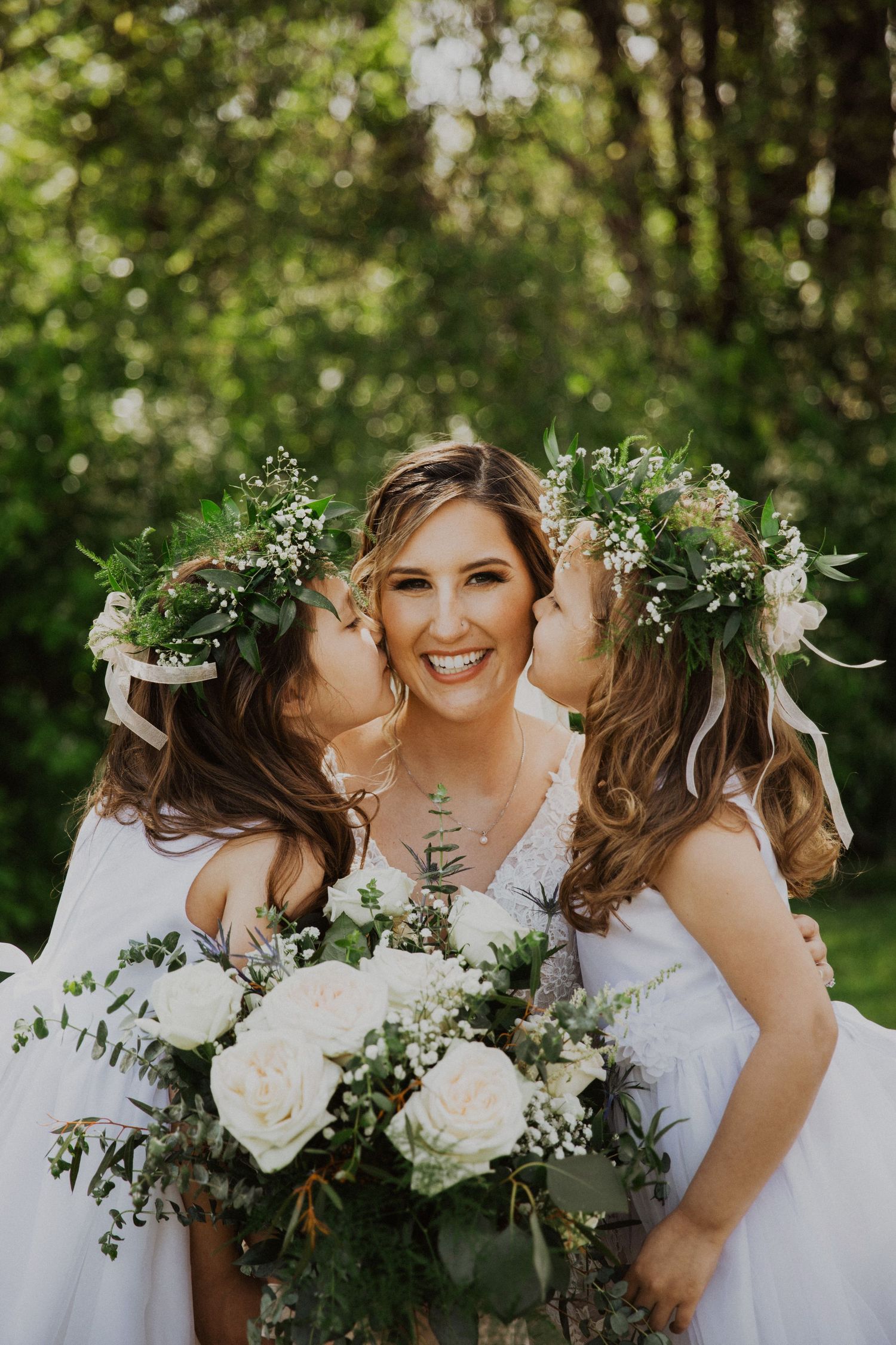 Bridesmaids in white dresses share a sweet moment with flowers and greenery.